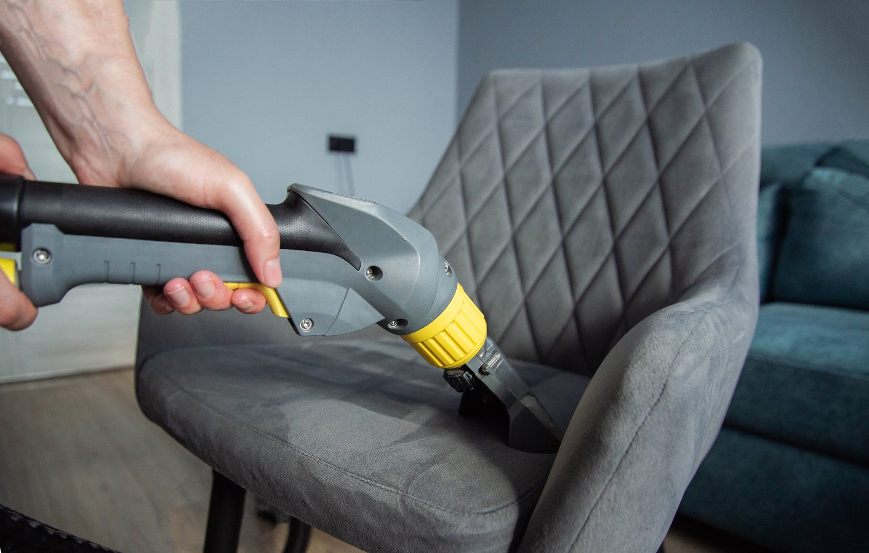 The hands of a girl with a washing vacuum cleaner clean and wash the gray upholstery of a soft chair from dirt. Cleaning services, business. Copy space for text