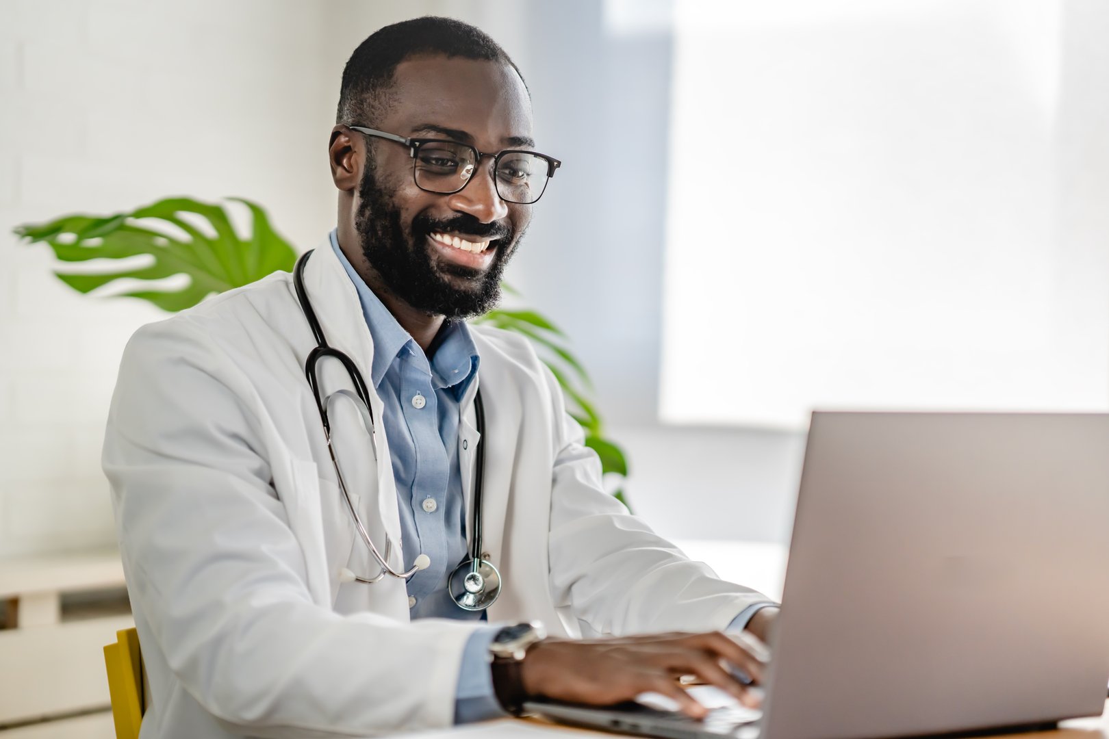 Smiling African-American doctor having an online consultation on his laptop in a bright, modern office. He appears engaged, communicating effectively with a patient.