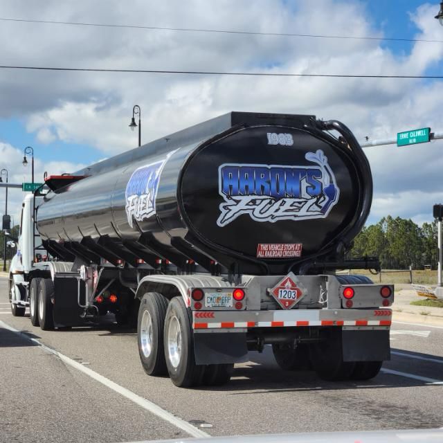 A black fuel tanker truck on a street, displaying "Babine's Fuel" logo and "1203" hazardous material sign.