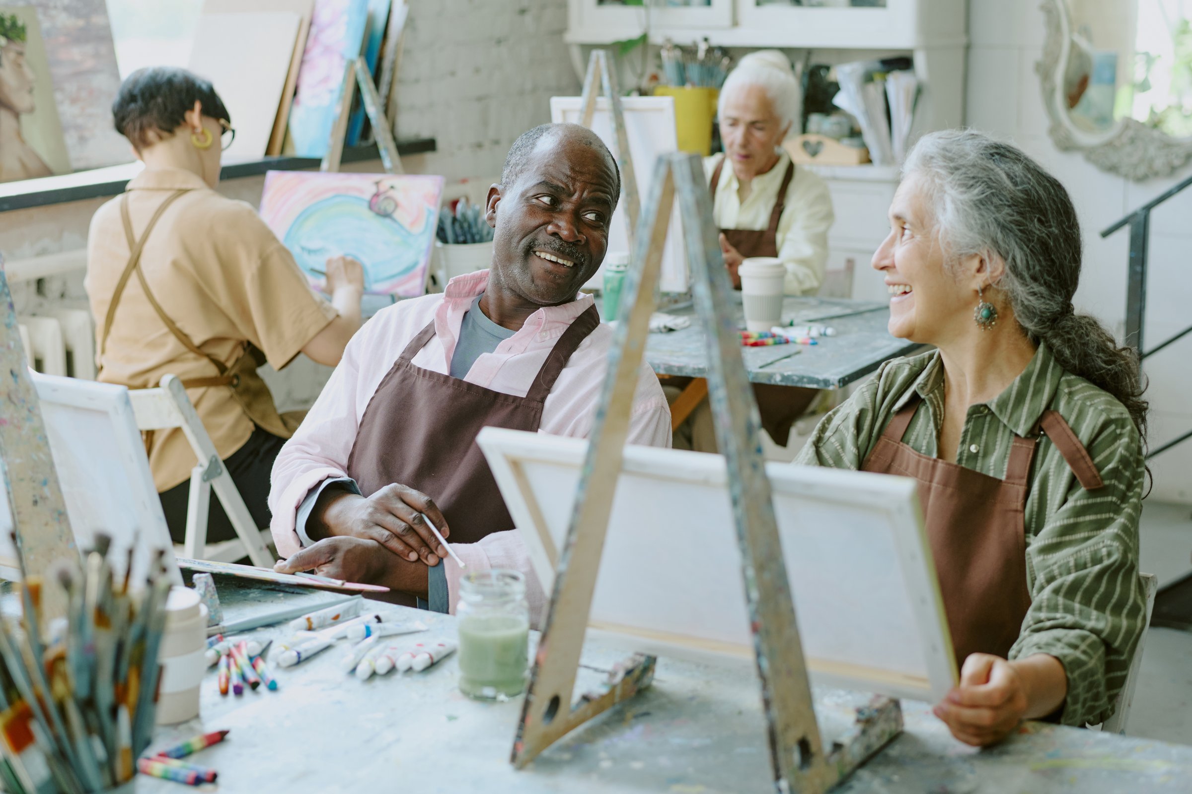 High angle shot of biracial senior couple chatting lovely while attending art therapy together in modern spacious drawing studio