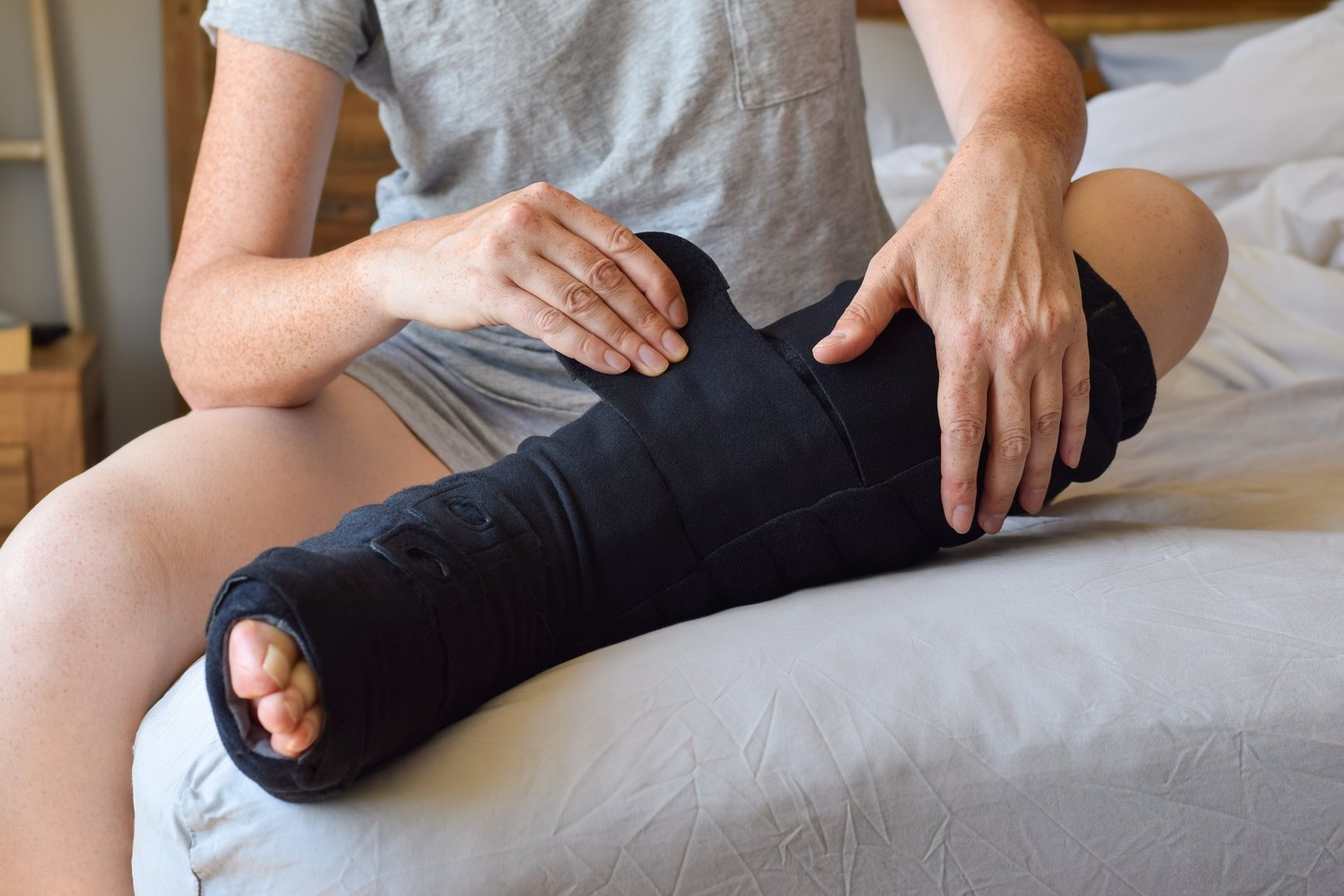 Woman sitting on bed putting on night compression wrap boot on lymphedema affected leg adjustable with velcro
