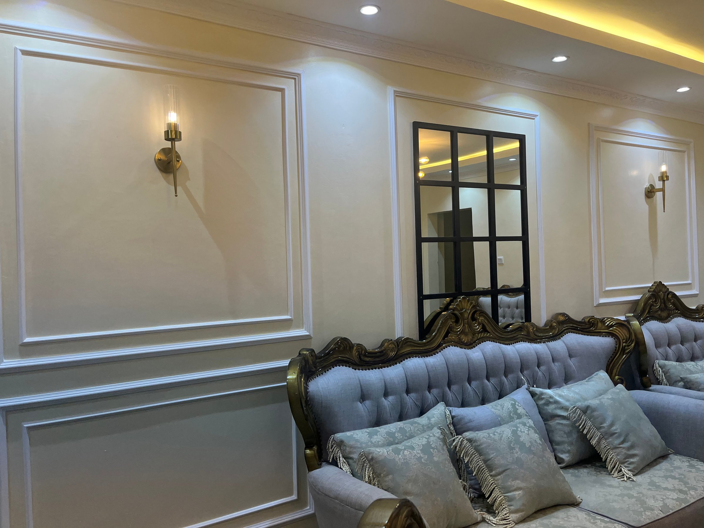 Elegant living room with ornate sofas, gray cushions, wall sconces, and a large mirror.