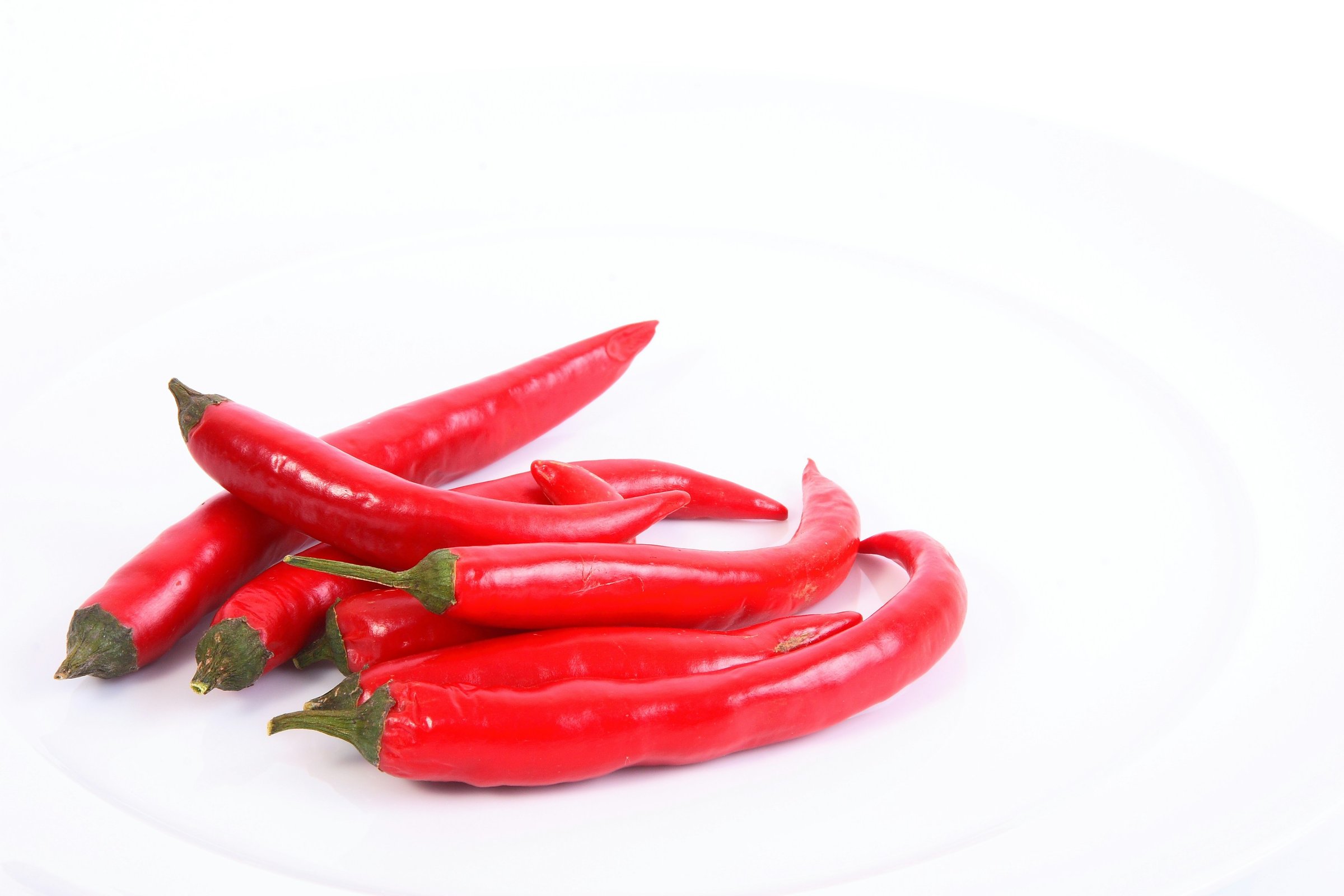 A group of red chili peppers on a white plate, arranged with their stems facing outward.