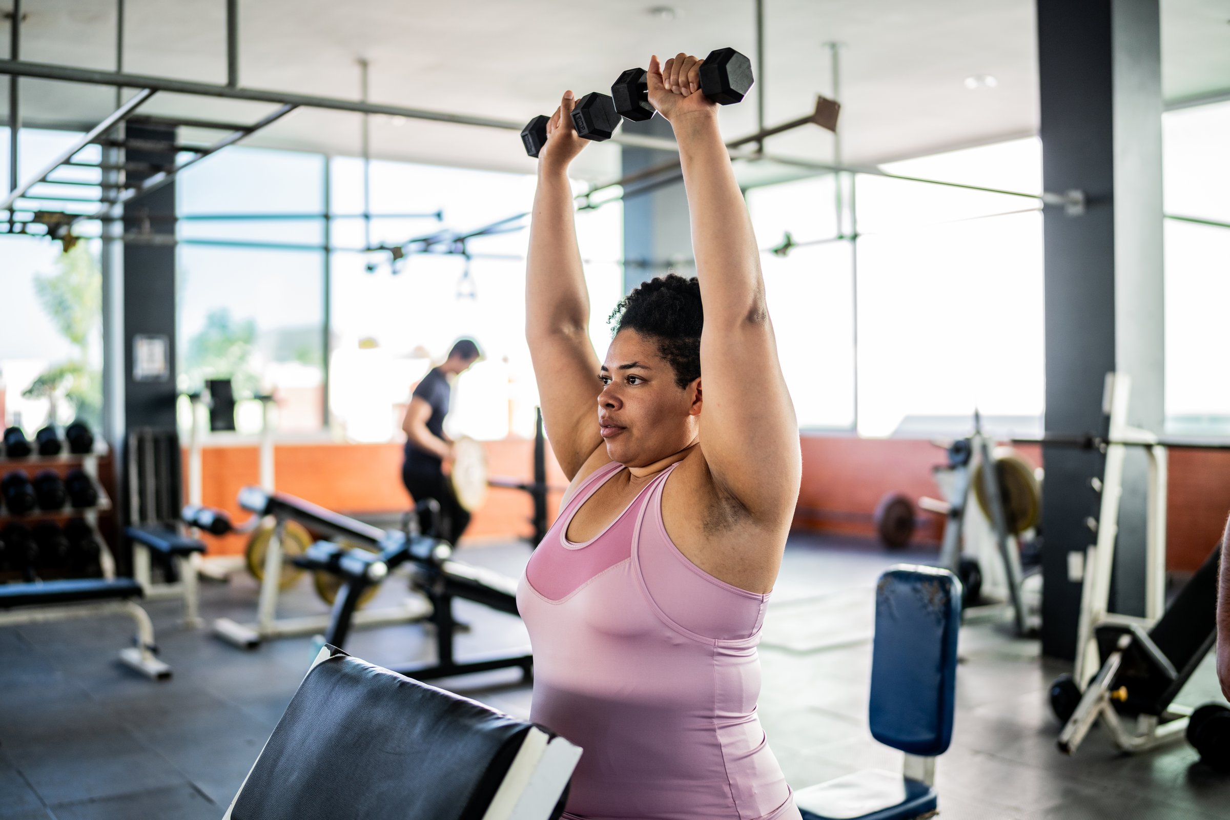 Mid adult woman doing shoulder exercise with dumbbell at gym
