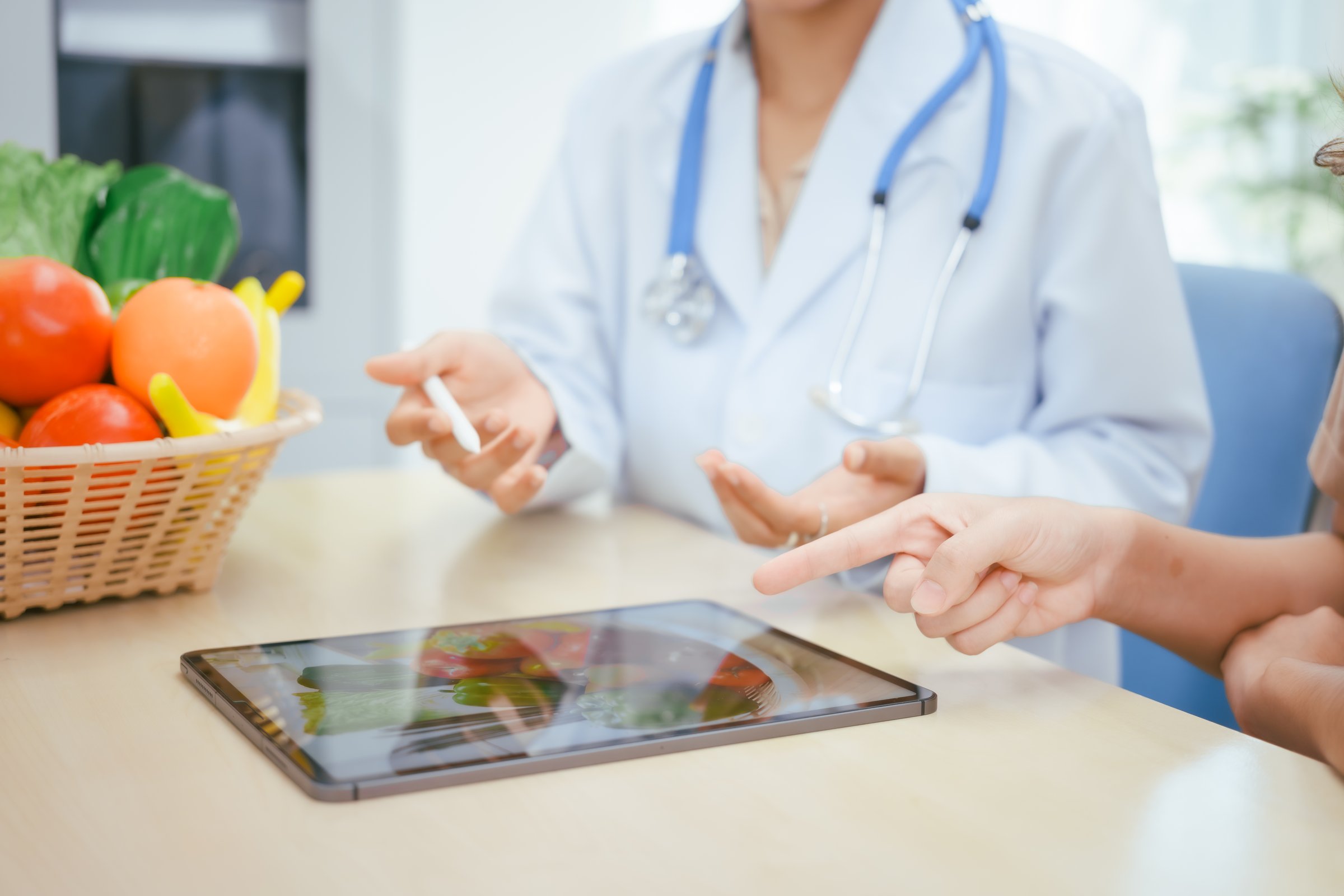 A young female nutritionist expert talks to a female patient at a table, recommending a healthy diet with vegetables and fruits to promote wellness, balanced nutrition, and effective weight loss