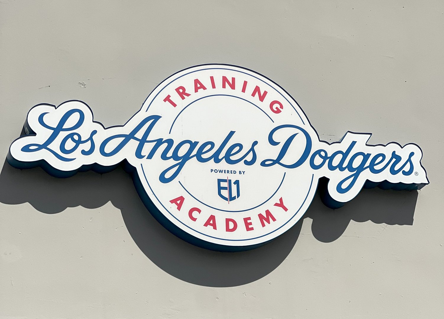 Sign for Los Angeles Dodgers Training Academy, powered by EL1, with a blue and red color scheme on a gray background.