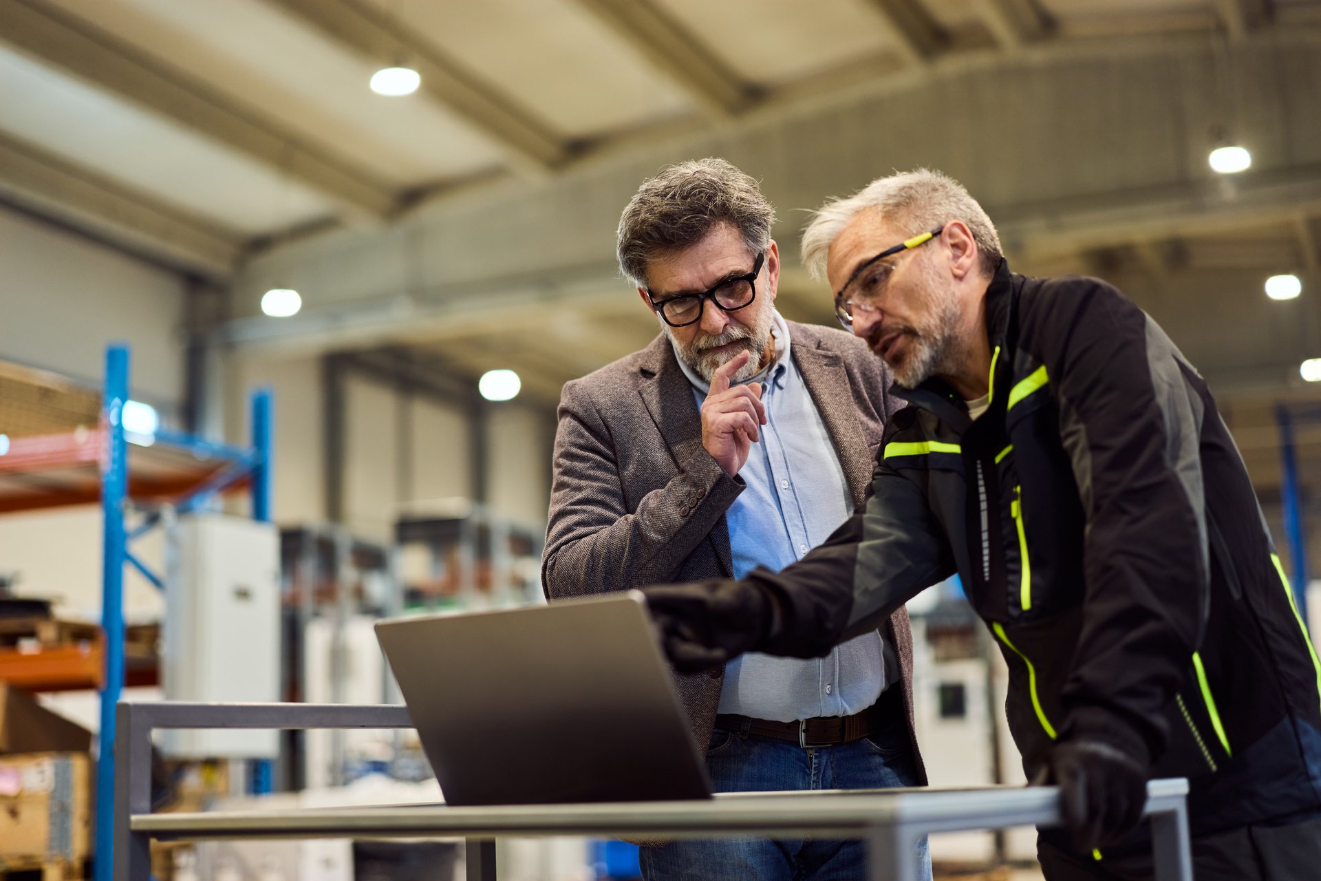 Two professionals discussing project details at a workstation in a factory environment
