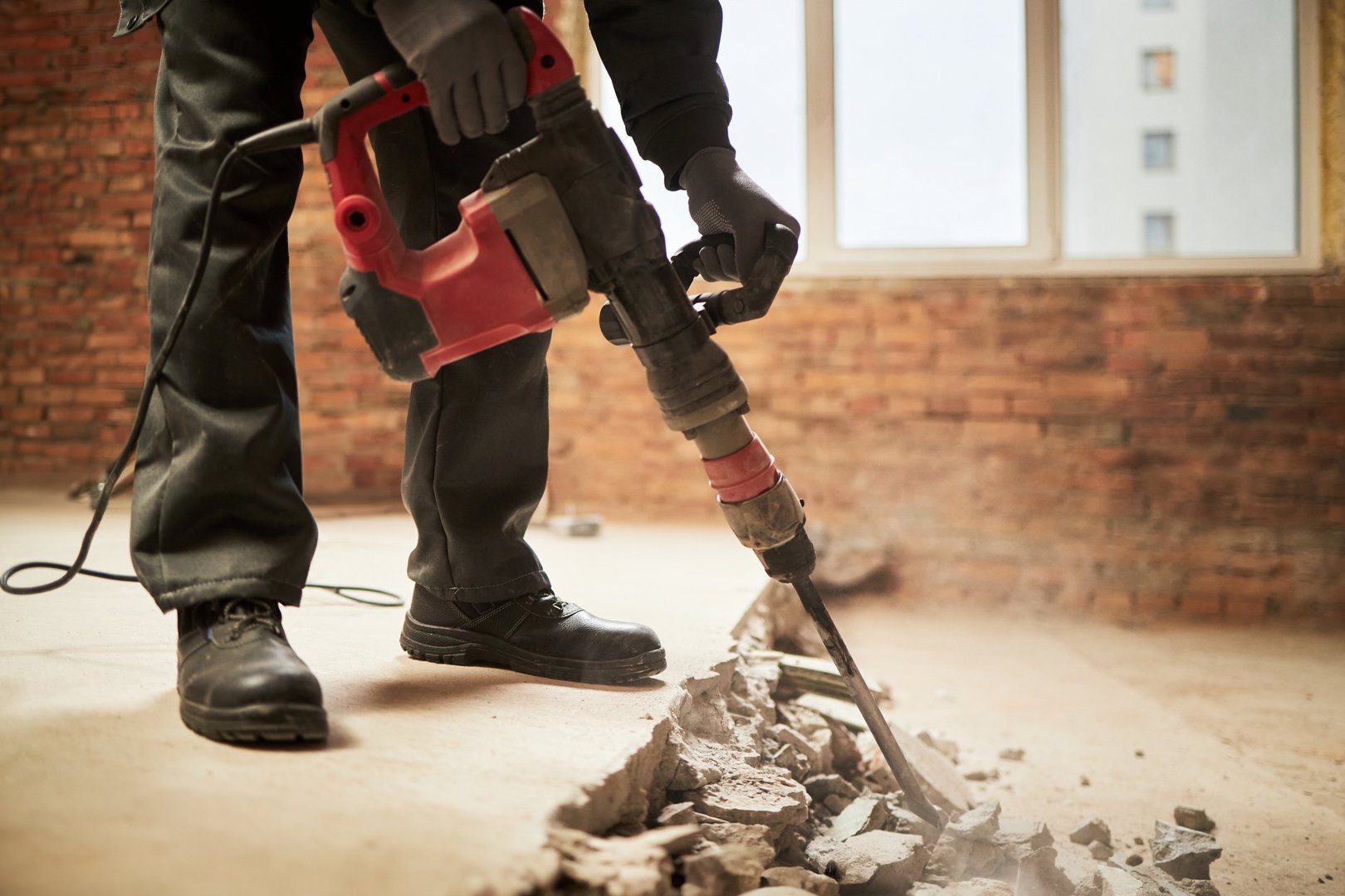 Medium close up of unrecognizable laborer destroying floor with massive jackhammer in room