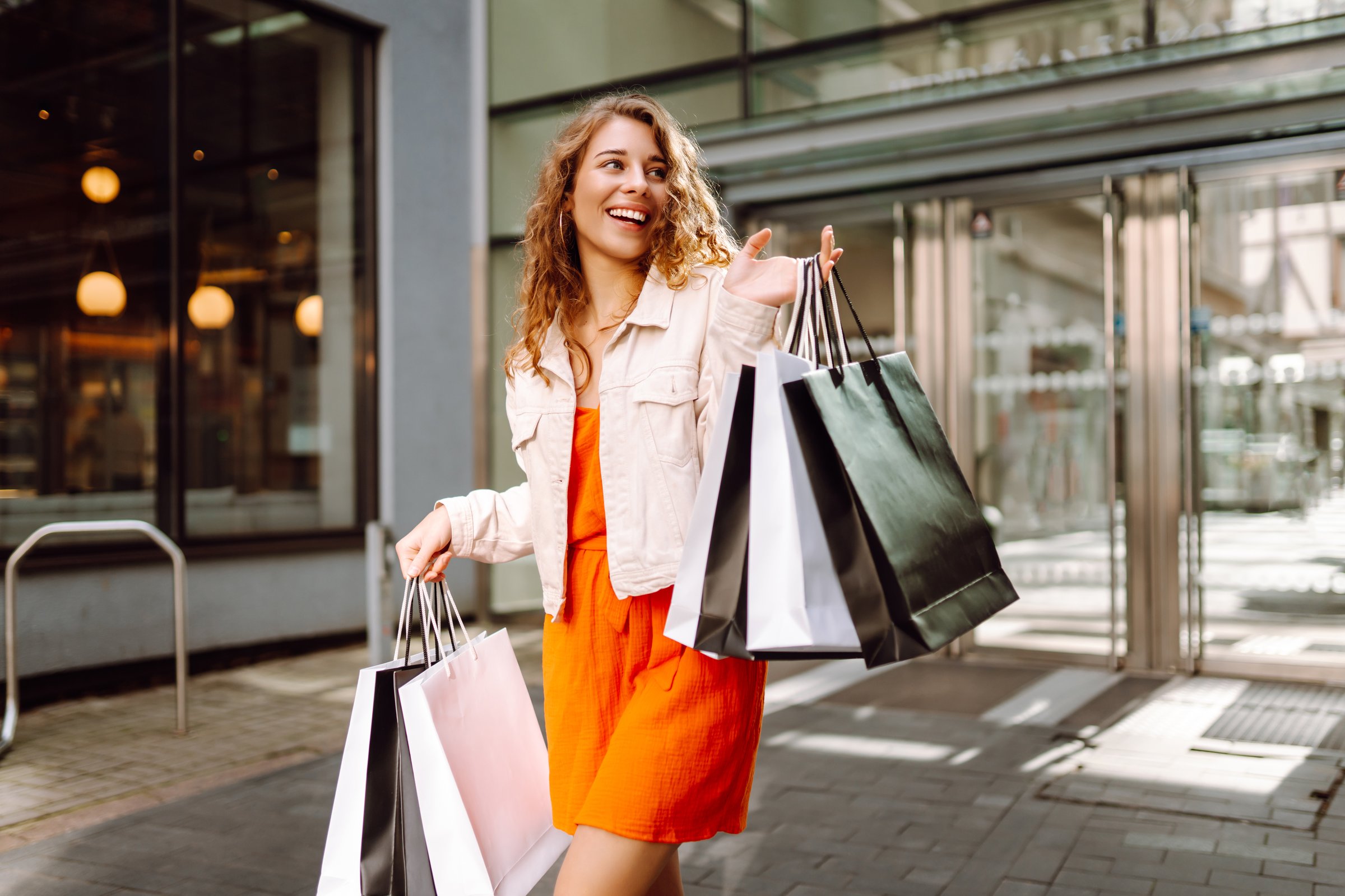 Cheerful woman enjoying shopping on a sunny day while carrying multiple bags in an urban setting. Consumerism, fashion, purchases, shopping, lifestyle concept.