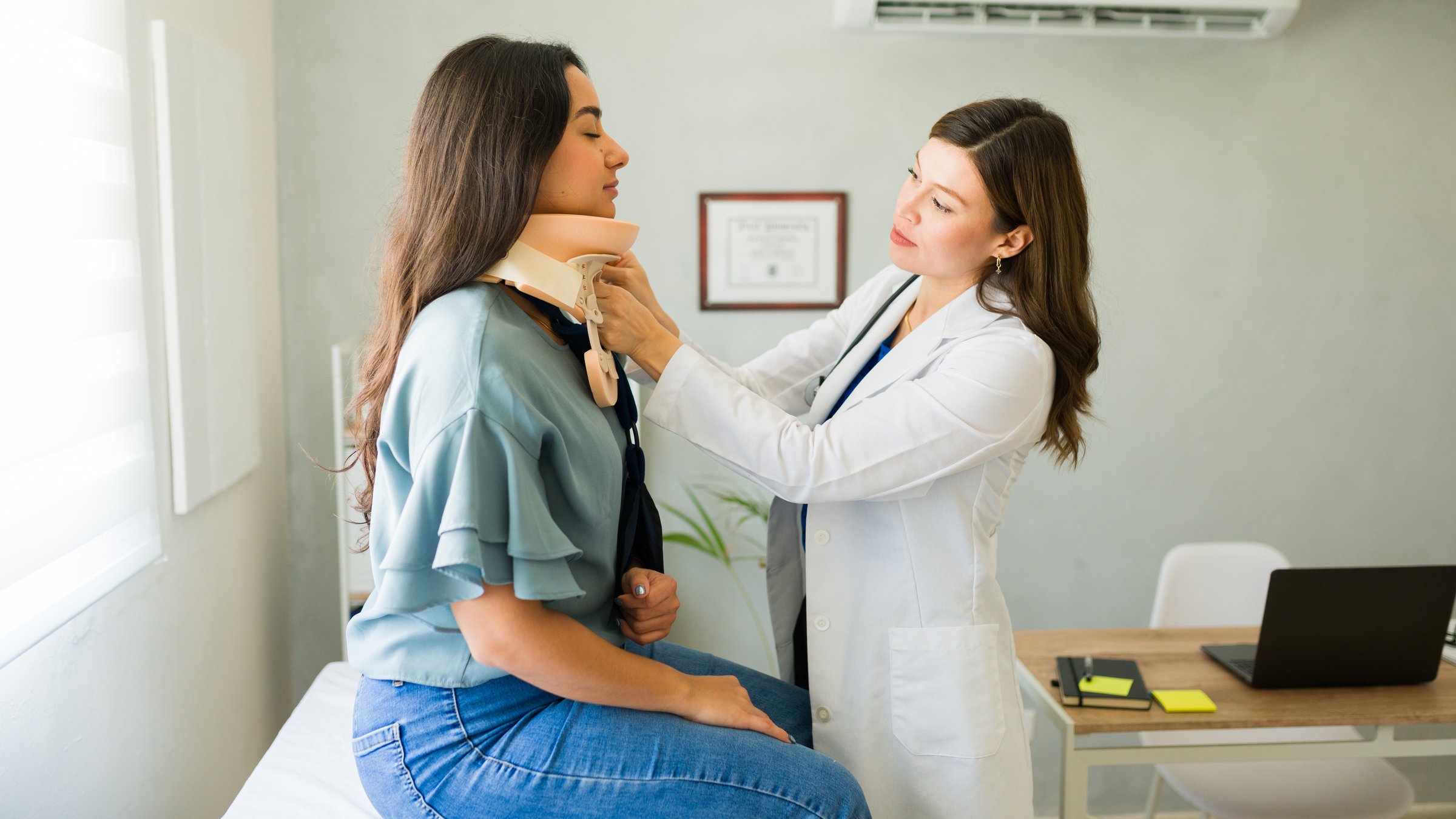 Good looking doctor is adjusting the cervical collar of a female patient who is sitting on an examination table