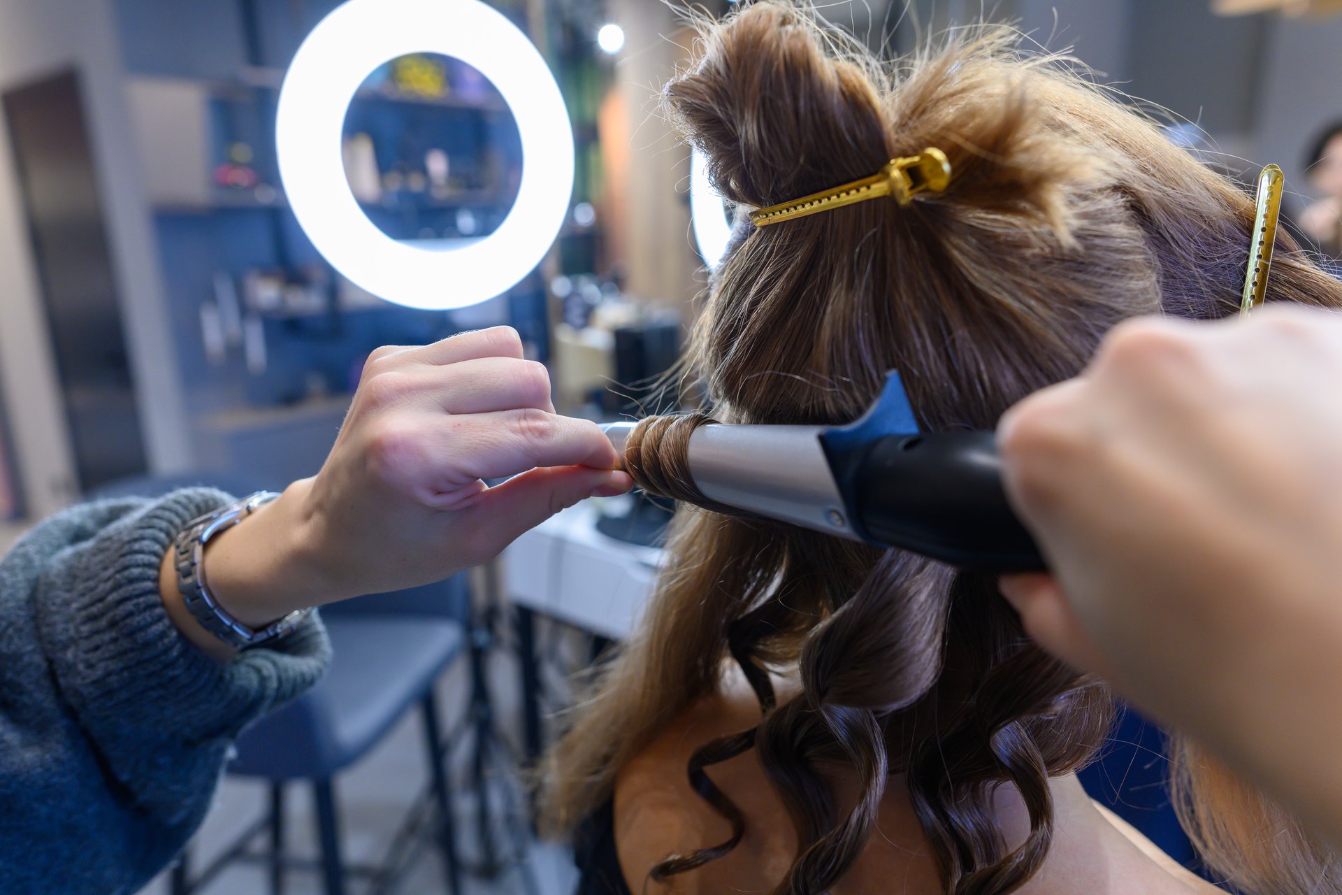 A stylist skillfully curls hair in a trendy salon, surrounded by bright lights and a chic atmosphere.
