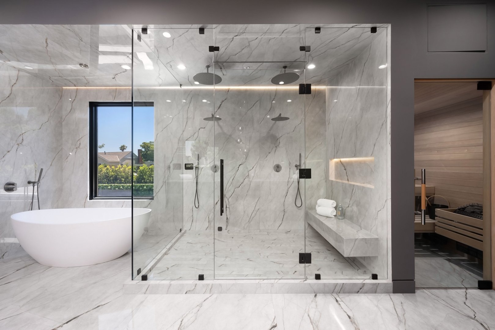 Modern luxury bathroom with a large glass shower, freestanding tub, and sauna, featuring marble walls and floors.