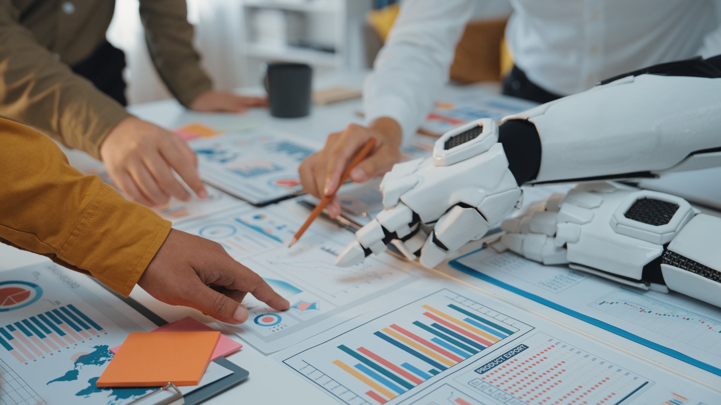 A dynamic business meeting scene showcasing human and robotic hands working together, analyzing financial charts and graphs to make informed decisions in a modern office setting.Noogenesis
