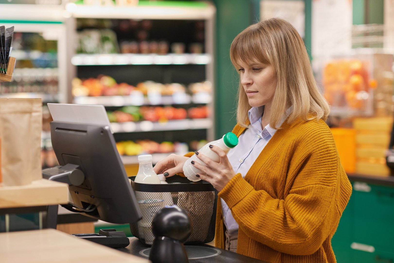 Waist up portrait of female customer using self checkout machine in grocery store and buying milk copy space