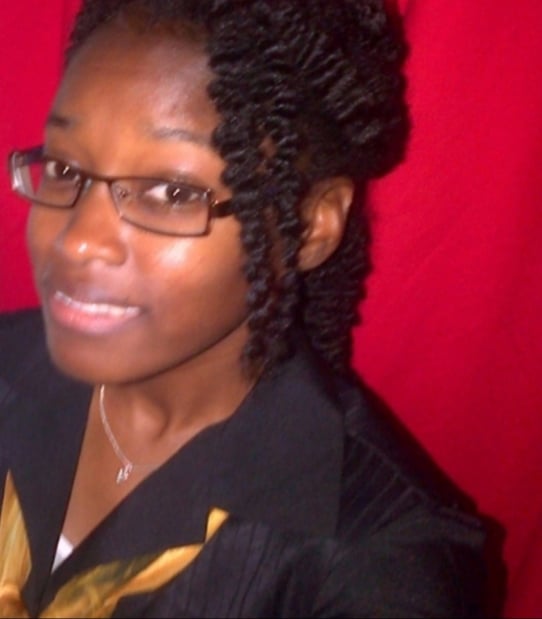 A person wearing glasses and a black top smiles against a red background.