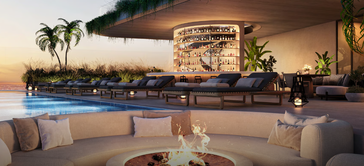Luxurious rooftop pool area with lounge chairs, circular fire pit, and a curved bar illuminated at sunset.
