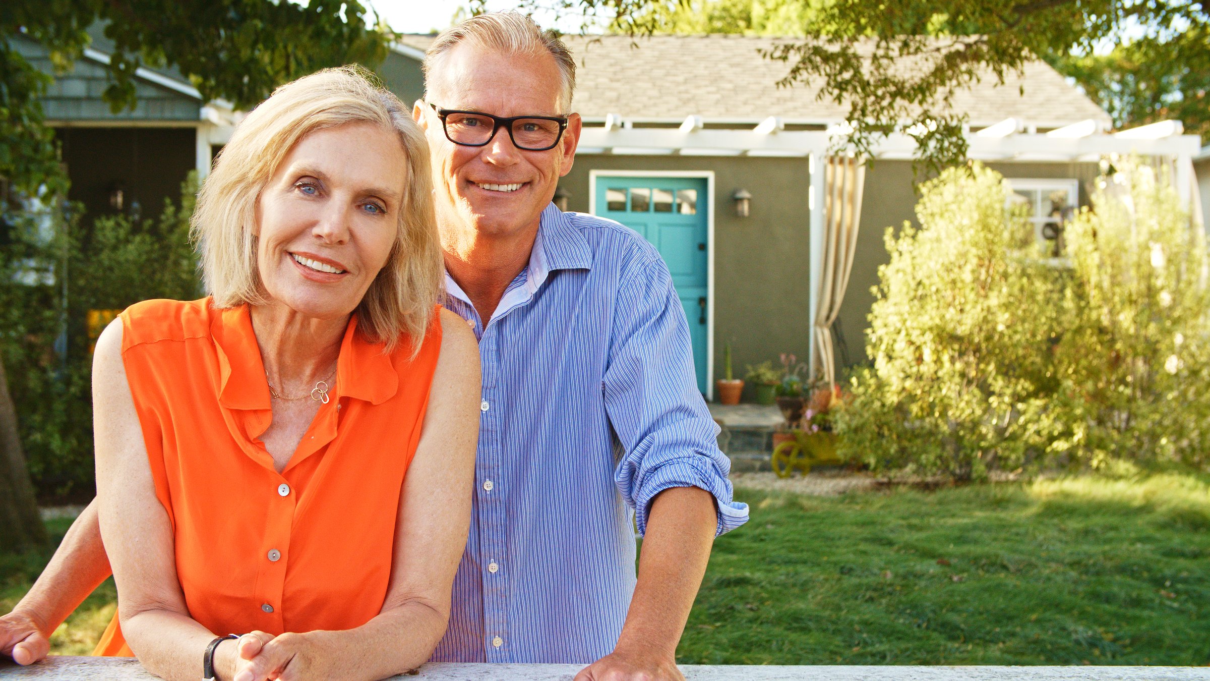 Portrait Of Smiling Mature Couple At Home Looking Over Back Yard Fence