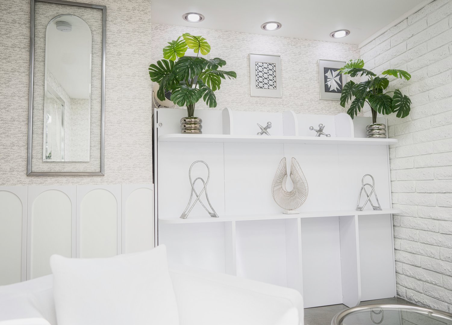 Stark white ultra-modern room with chrome art and green plants on a shelf, flanked by a vintage mirror and a white brick wall for a sleek curated look.