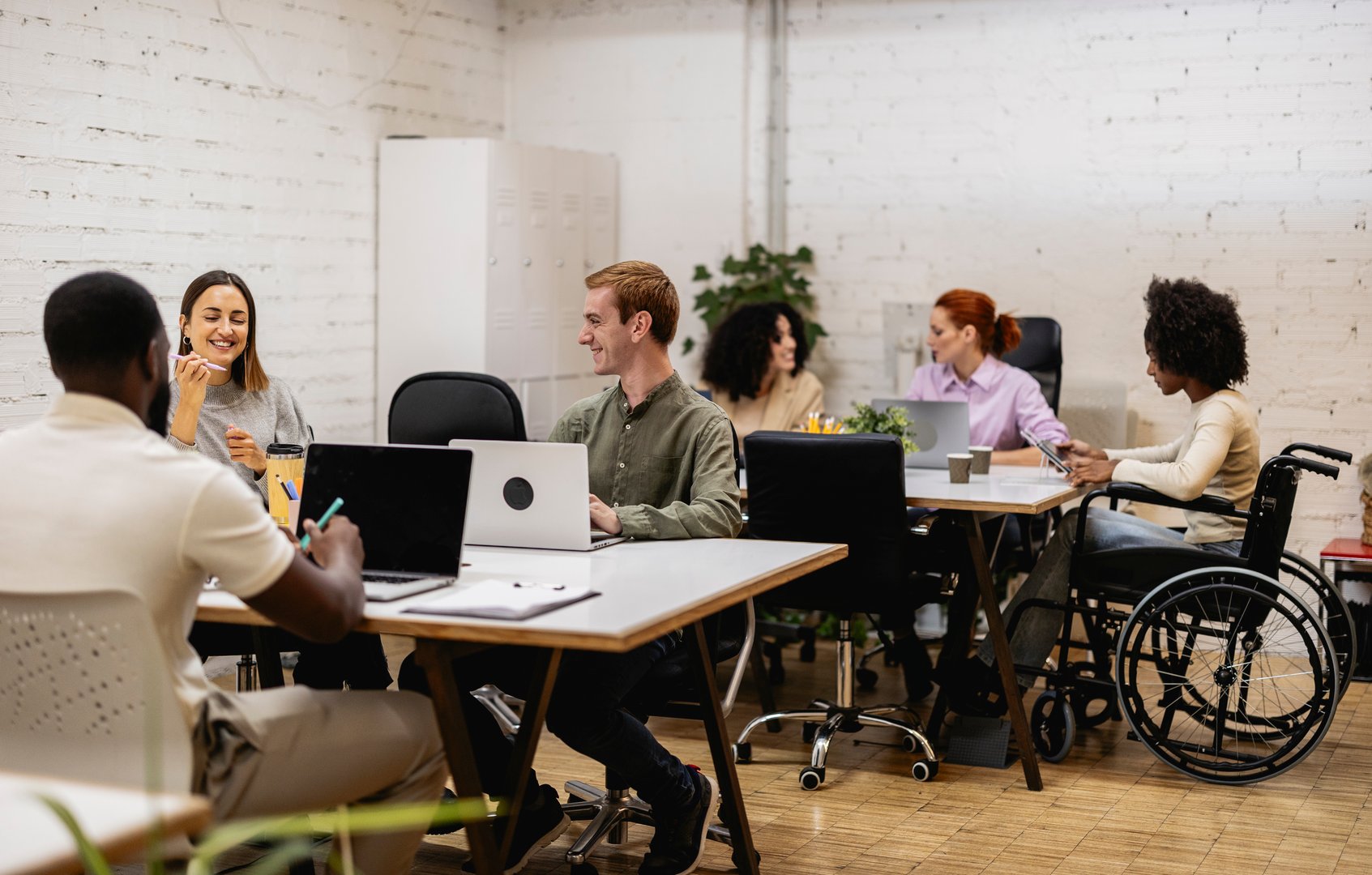 Multiracial team working together in a bright, modern office, showcasing diversity, inclusion, and collaboration in a professional environment, with a woman using a wheelchair