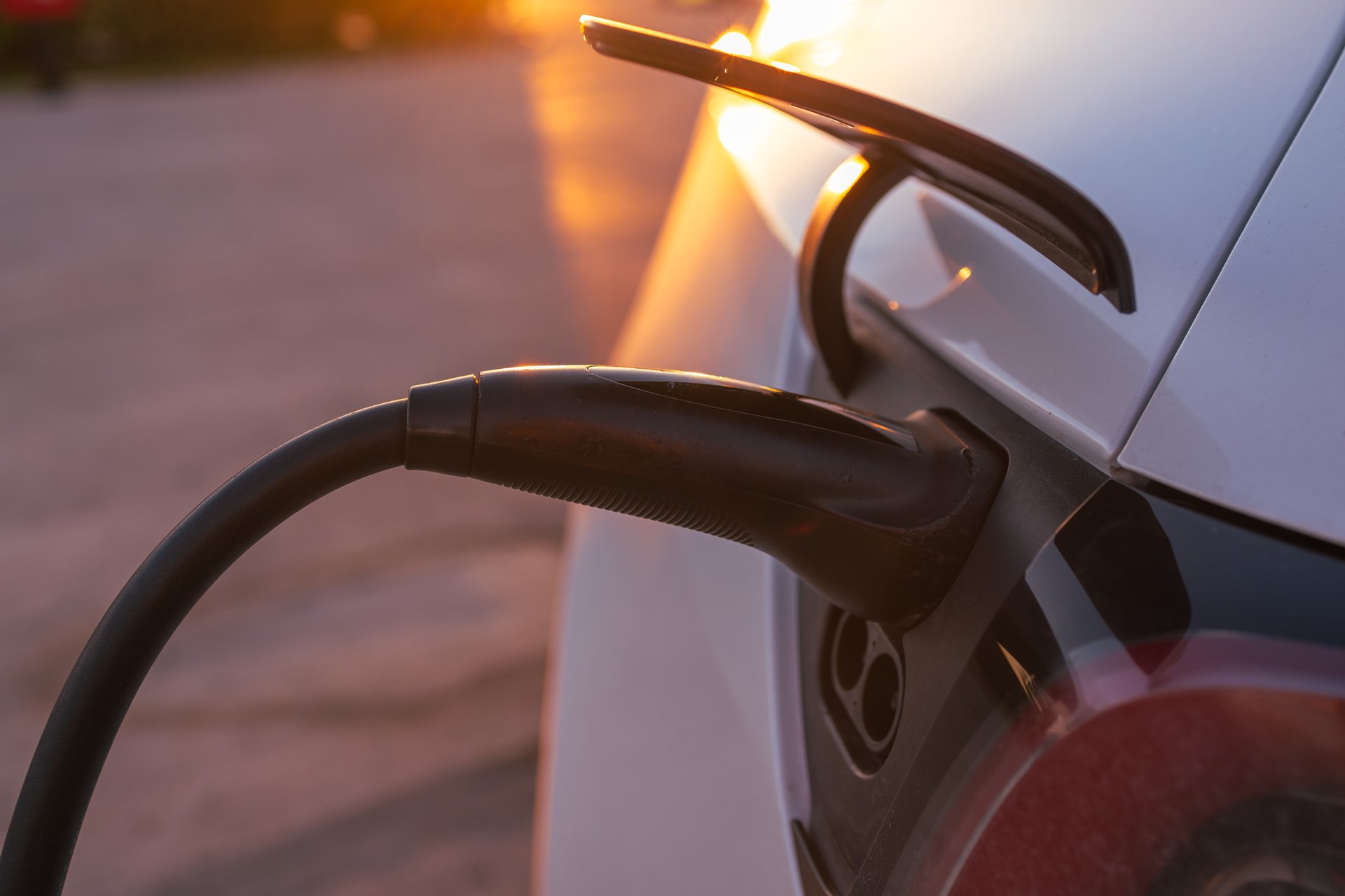 A detailed close-up of an electric car being charged, with the warm glow of the sunset in the background. The image emphasizes eco-friendly transportation, sustainable energy solutions, and the transition to renewable energy in a visually appealing setting.