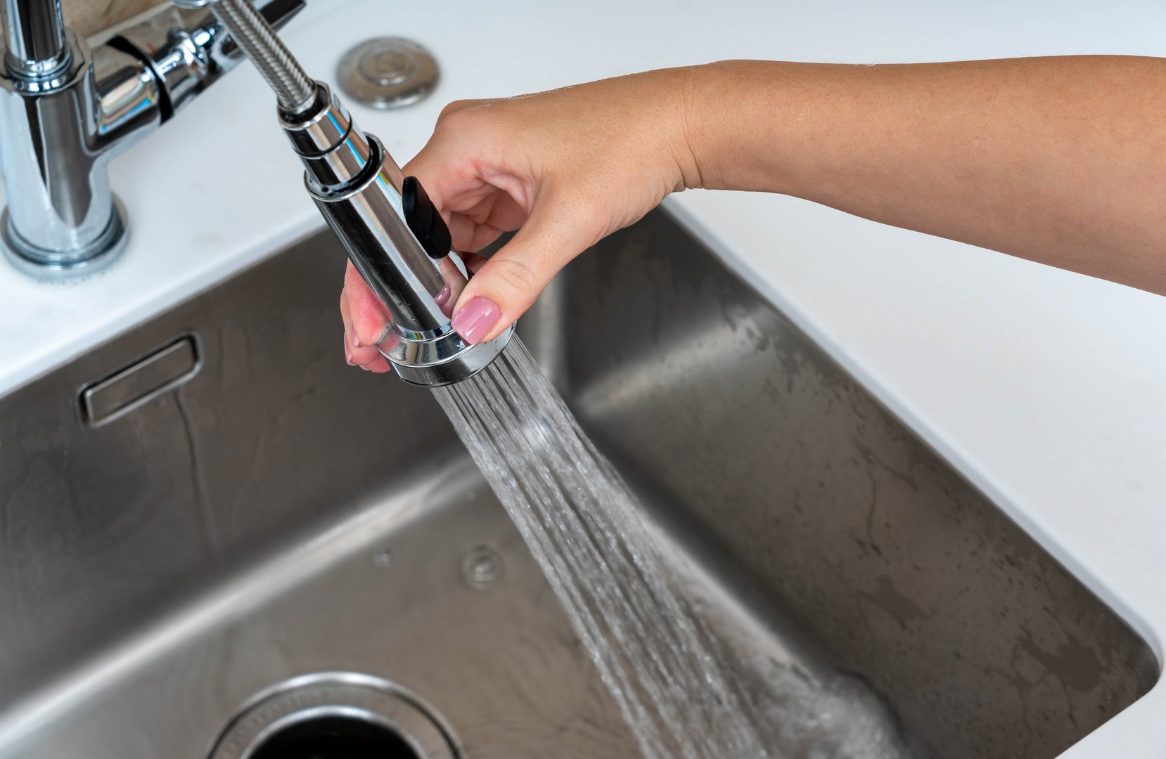 A person holding an adjustable faucet sprayer in a stainless steel sink, releasing a stream of water for cleaning purposes
