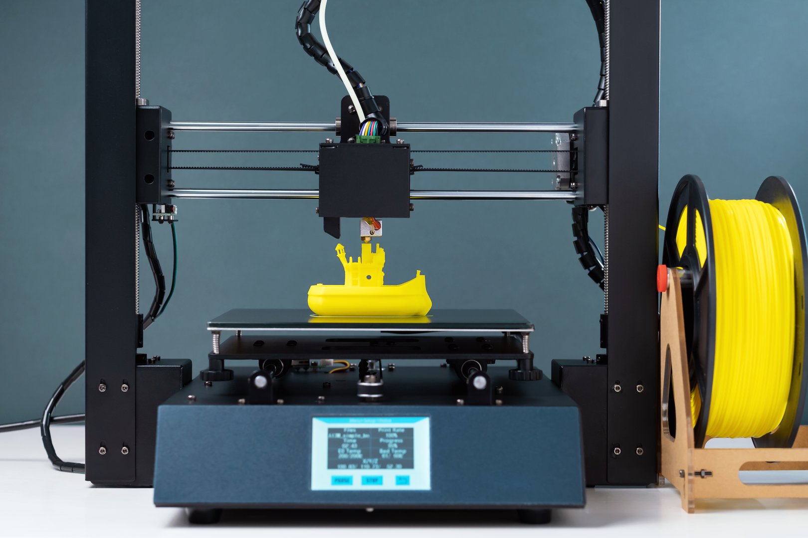 Printing on 3D printer figurines toys ship from yellow plastic close-up. Clear movements of the print head and printer working platform. Potential of modern technology 3D printing. Plastic reel