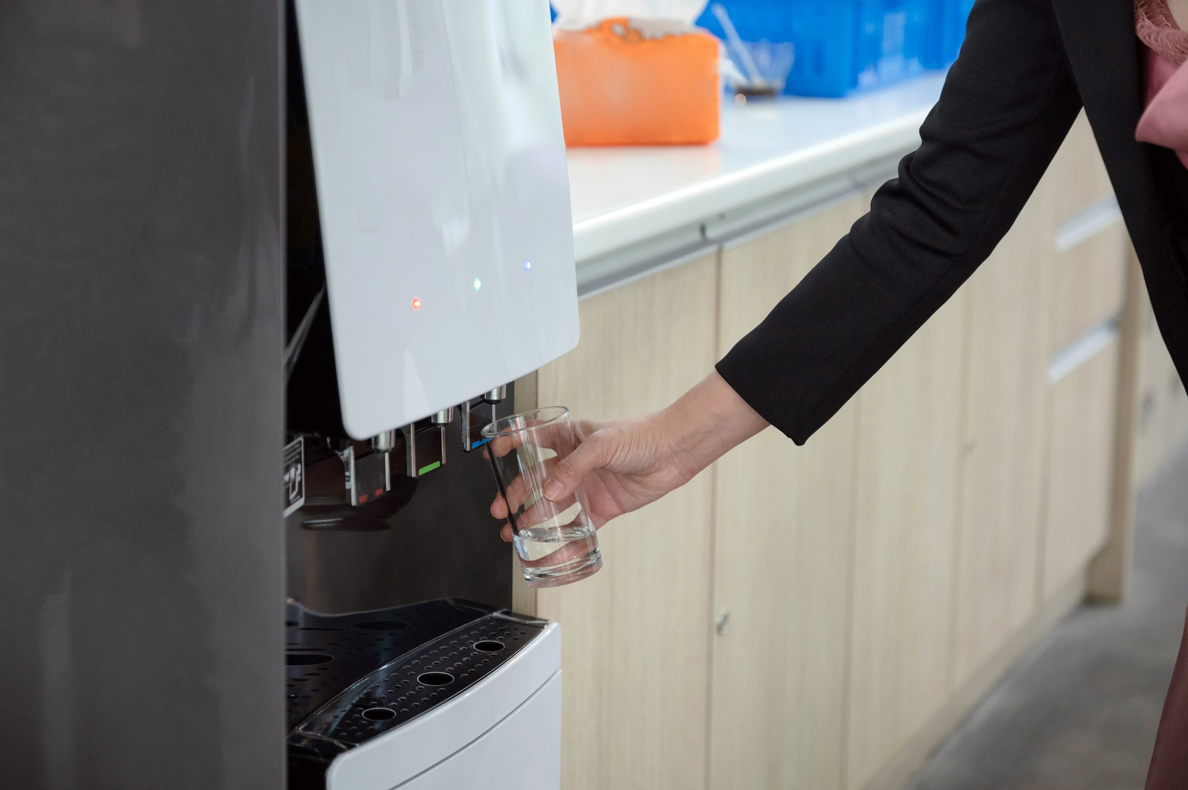 Woman hand holding glass filling cool water from water dispenser
