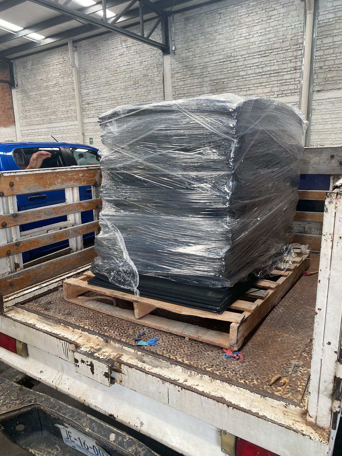 Stack of large black plastic sheets wrapped in clear plastic on a wooden pallet in the back of a truck in a warehouse.