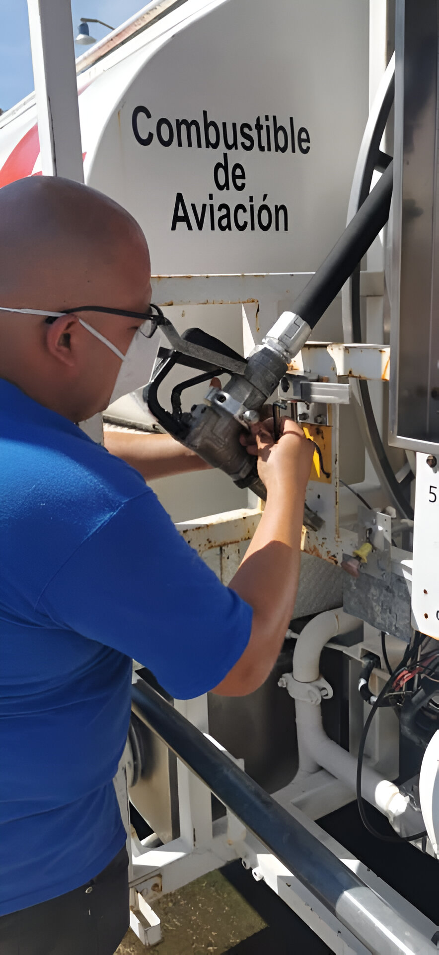 Person refueling an aircraft using a hose labeled Combustible de Aviación on a fuel truck.