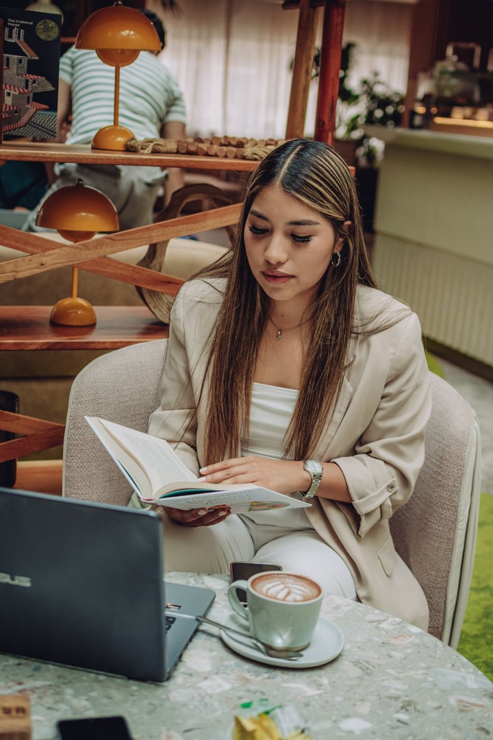 Woman with long hair and red lipstick, wearing a black t-shirt with a line drawing, stands with arms crossed in an office setting.