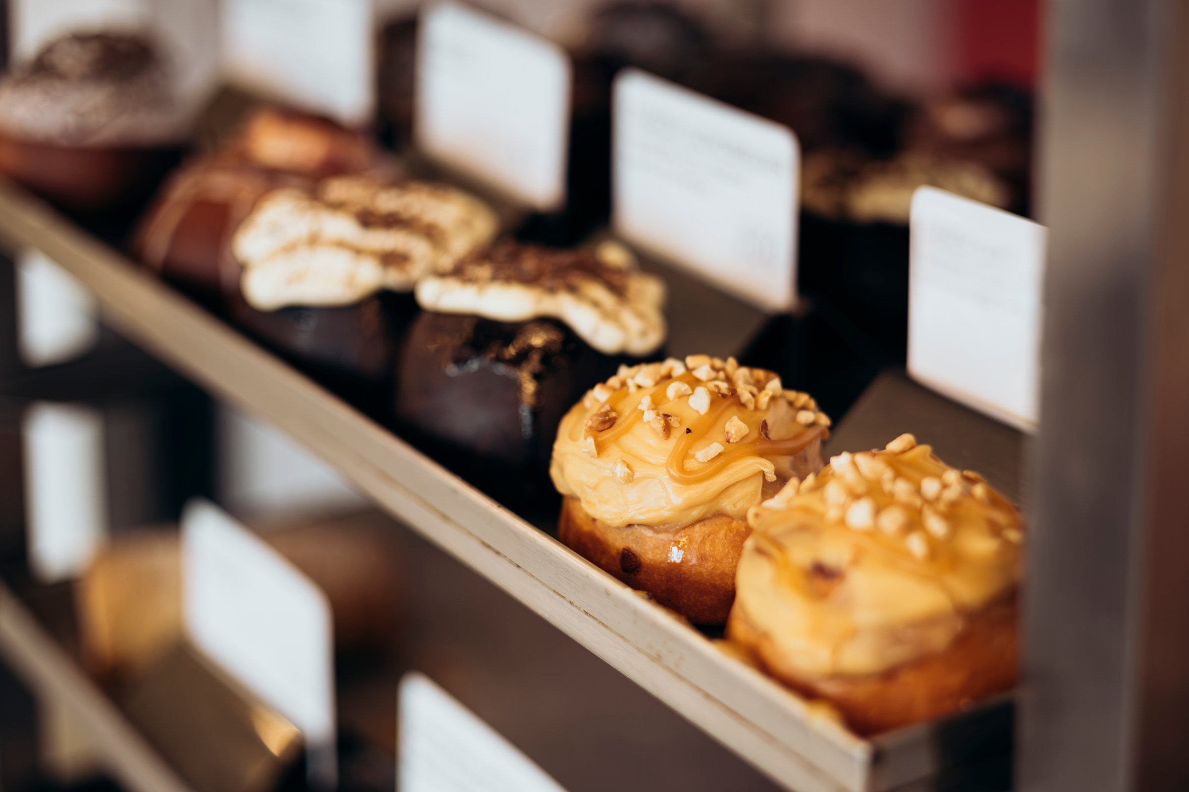 Appetizing cinnamon buns with cream in the bakery window. Freshly baked buns on display in a cafe. Freshly baked dessert buns in a bakery. Variety of cupcakes are displayed in a bakery window.