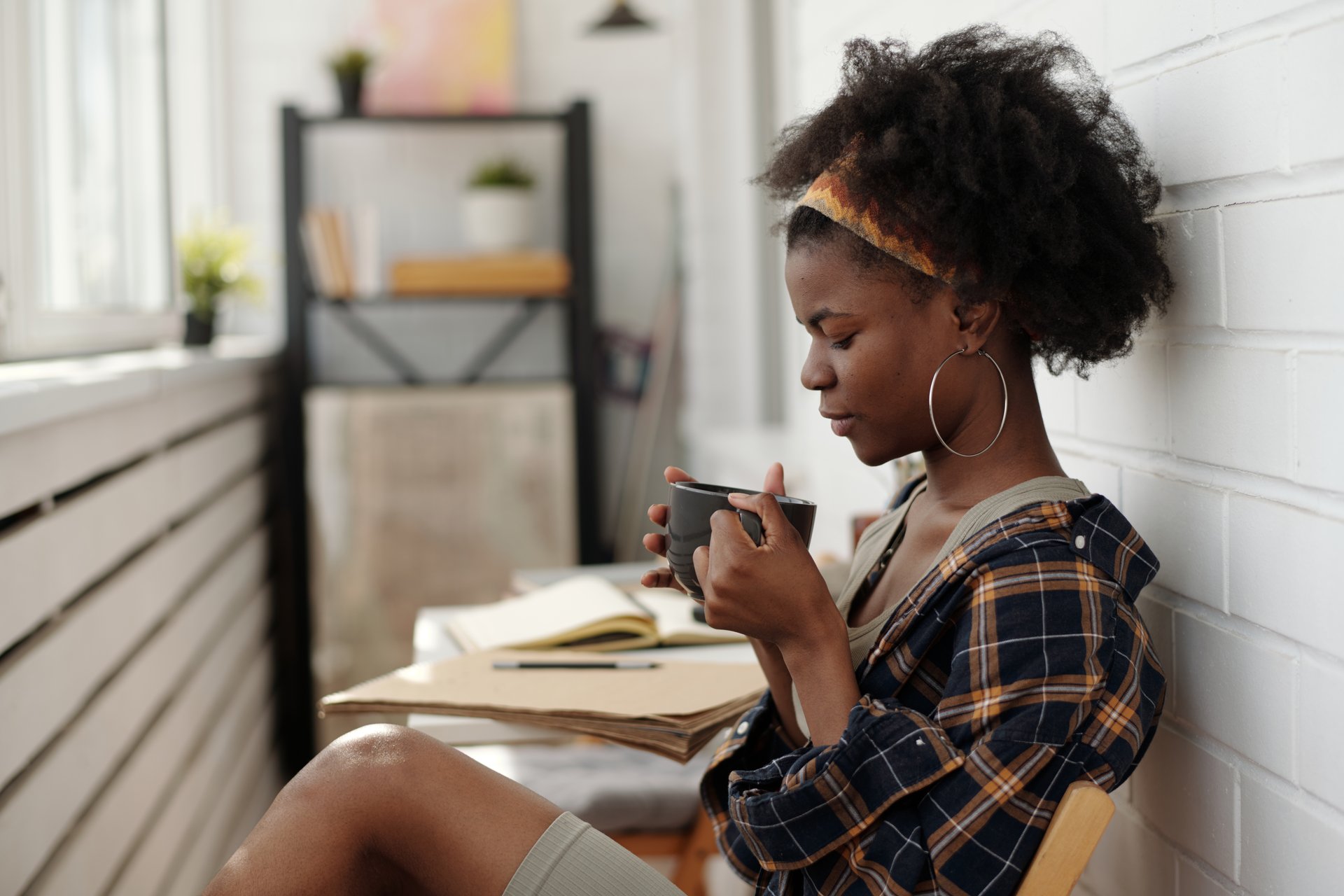 Person enjoying leisure time while sipping coffee and holding book. Relaxing near window with natural light streaming in and cozy ambiance surrounding them