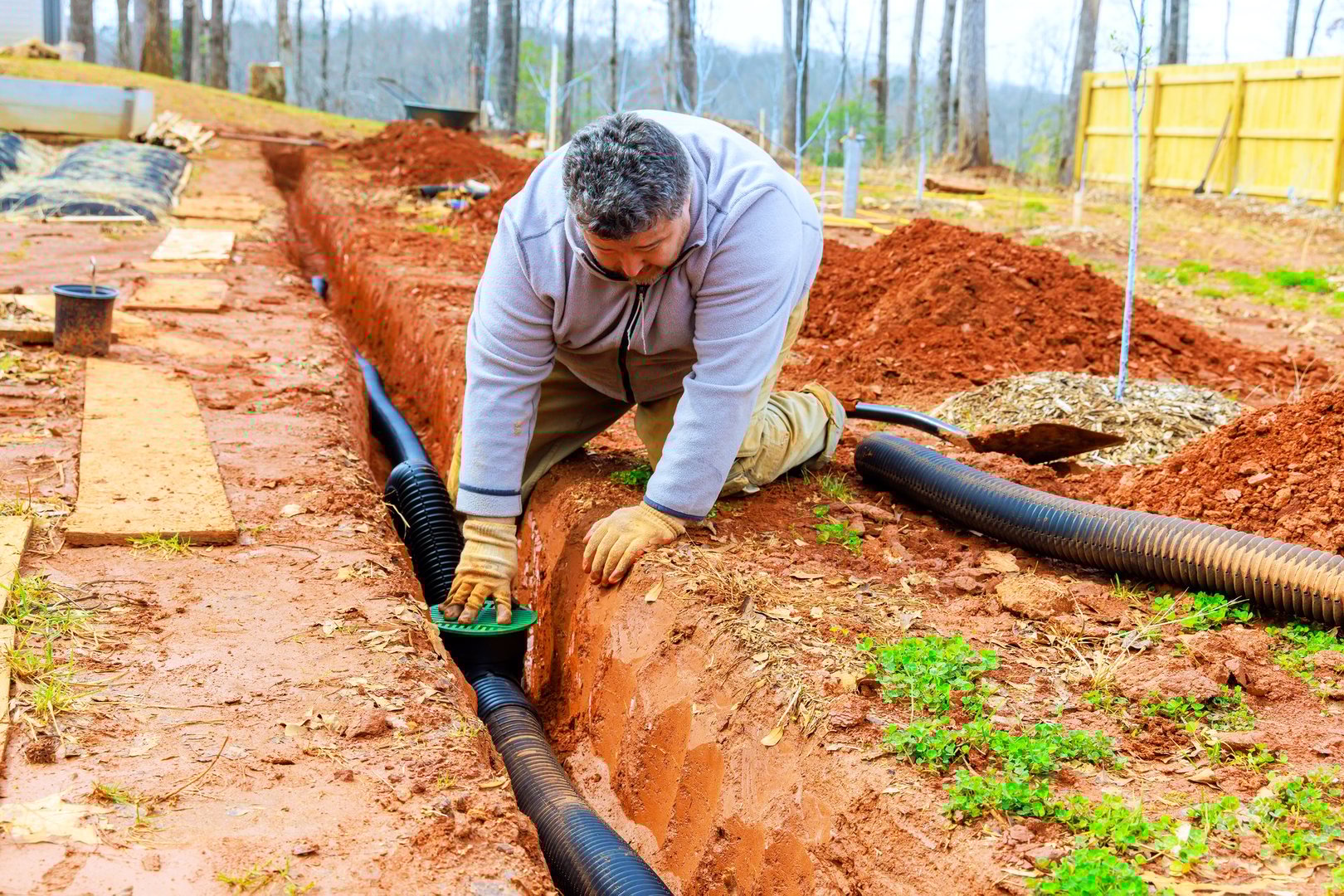 Man works diligently to place drainage pipes in trench, ensuring proper water management in residential backyard