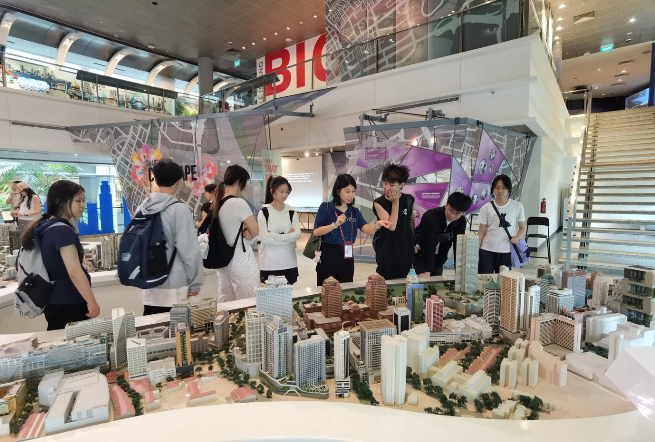 A group of people examining a detailed architectural model of a city inside a modern building with informational displays.