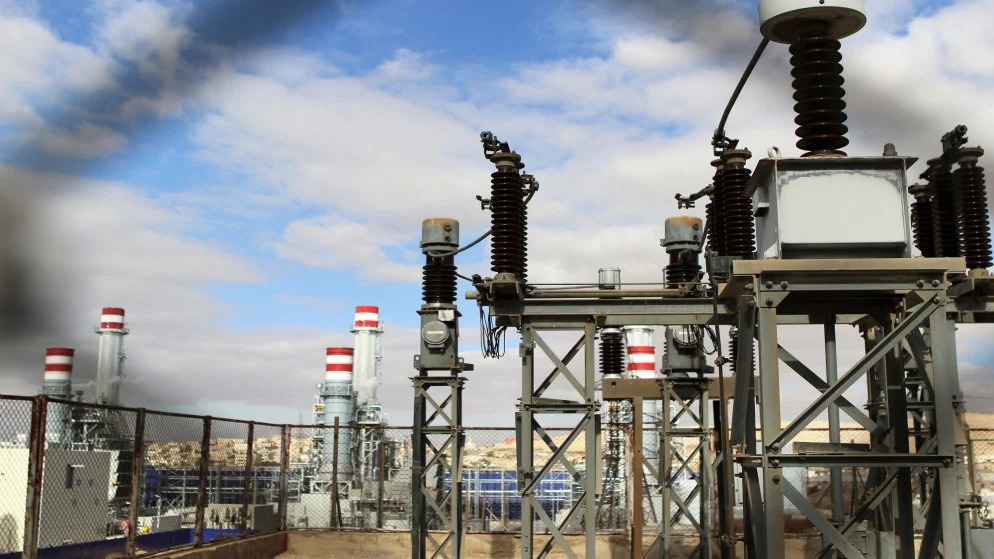 Industrial power station with electrical transformers and towers under a partly cloudy sky.