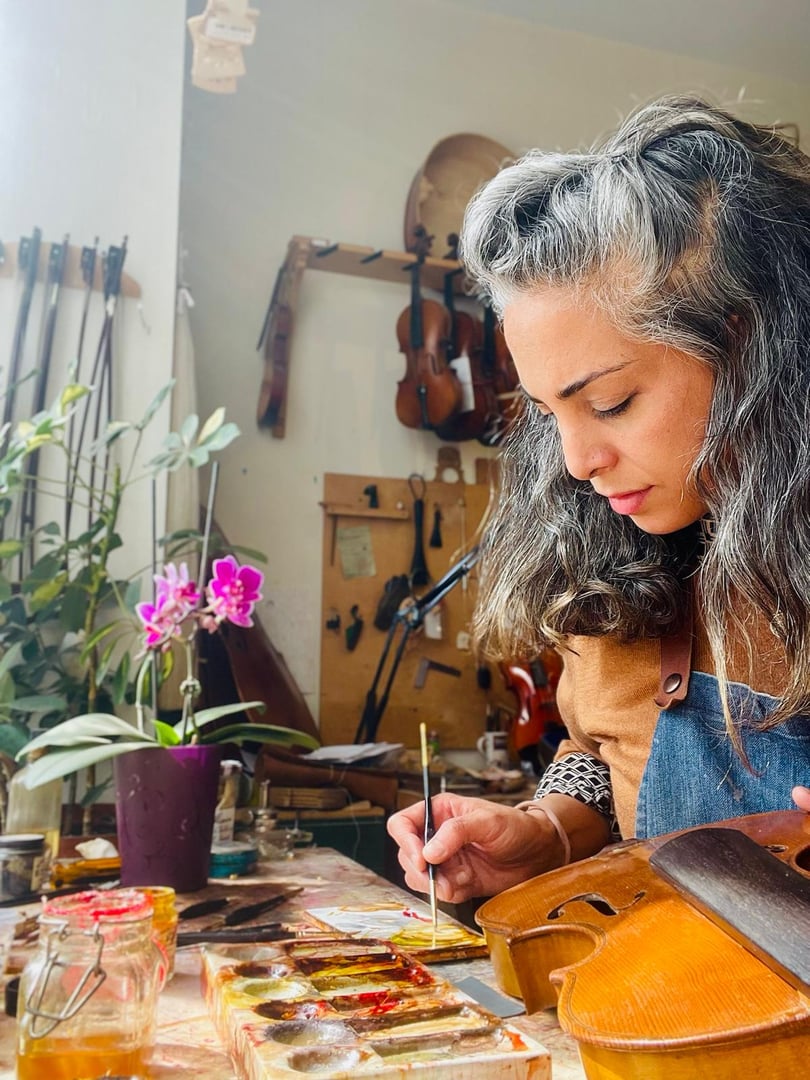 Luthier working diligently in a workshop, carefully assembling violin parts with specialized tools and techniques, showcasing craftsmanship and dedication to the art of instrument making