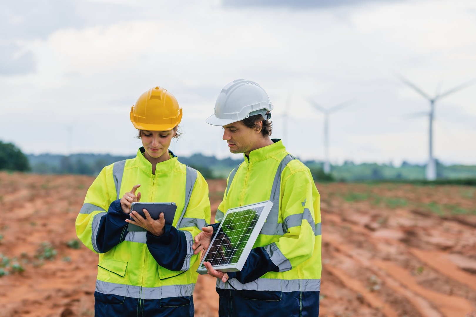 Two people wearing safety gear and holding tablets, looking at something on the screen. Scene is serious and focused
