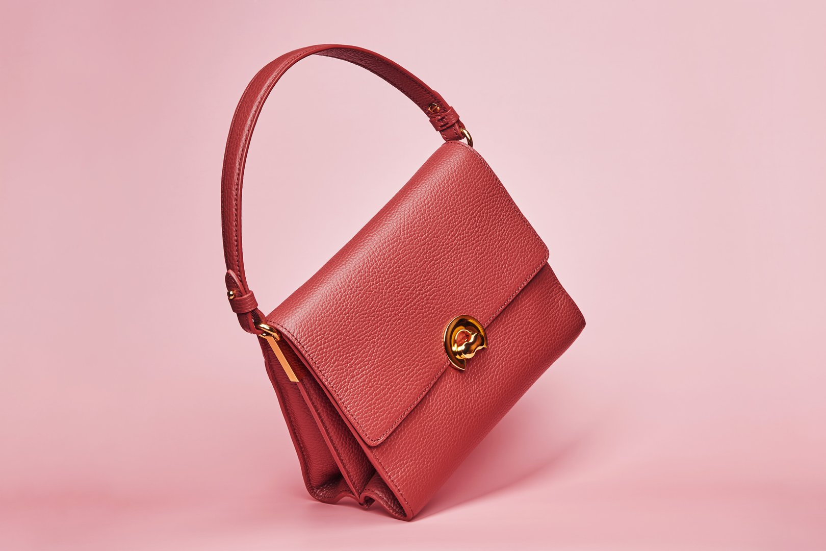 Luxury stylish women's female red brown leather hand bag isolated on the bright solid fond plain pink rose background. Fashion accessories concept