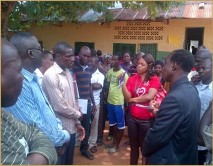 A group of people having a discussion outdoors, with one woman in a red shirt gesturing while others listen.