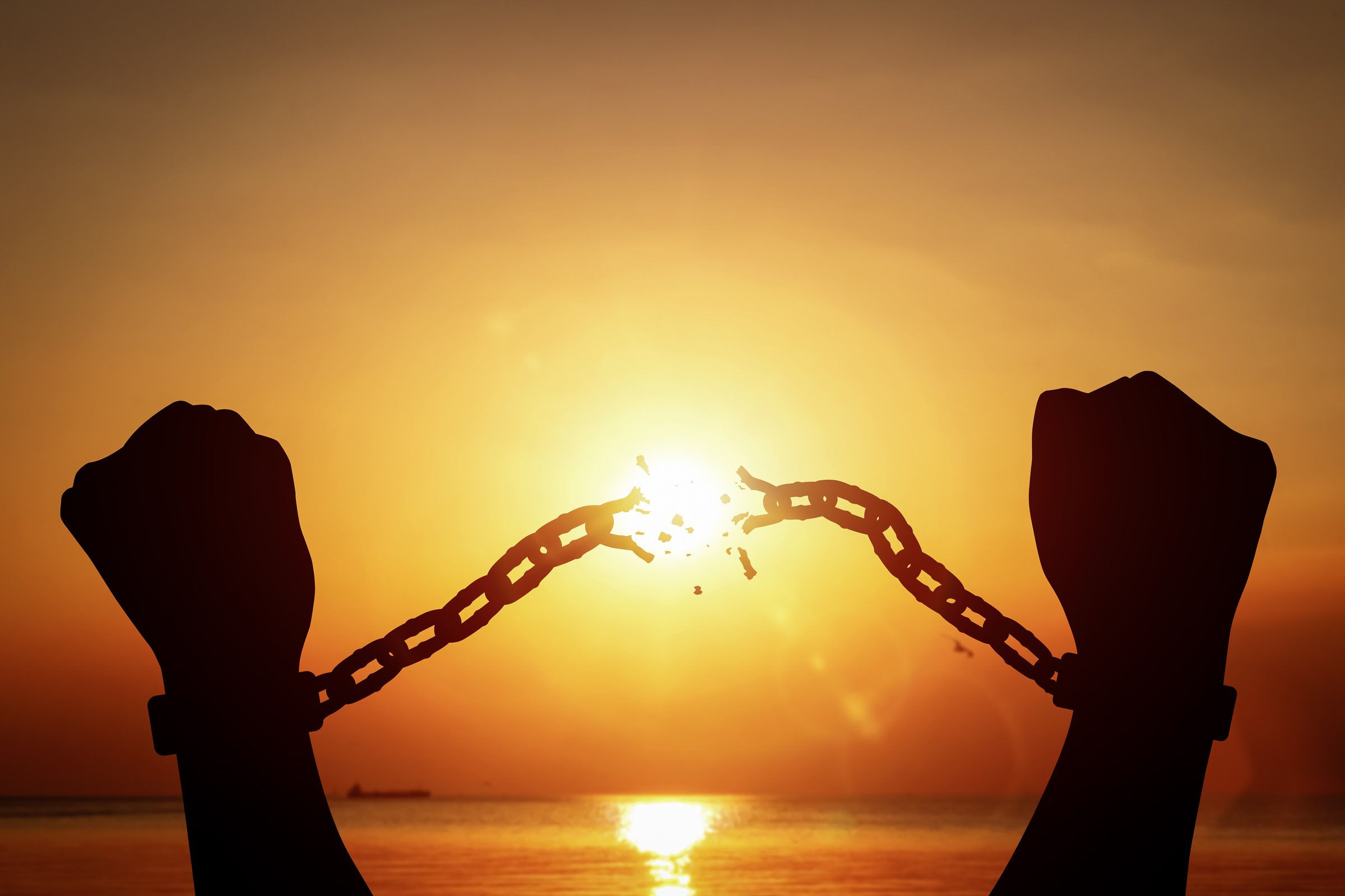 Silhouette of raised hands breaking chains on sunset background. Concept of fight for freedom, and overcoming limitations.