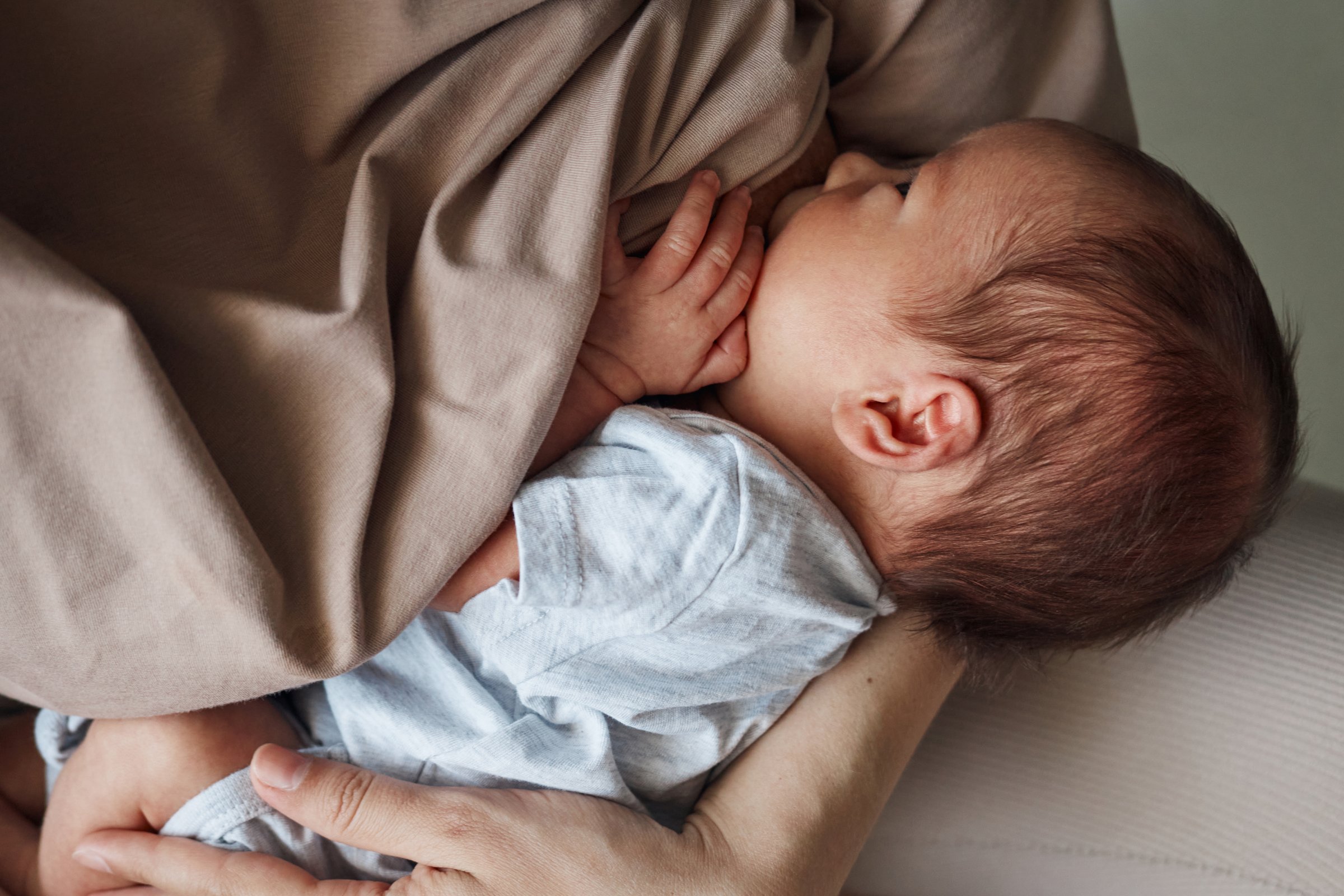 Home breastfeeding routine. Home lactation support. Comfortable nursing space. Unrecognizable woman young mother breastfeeding her baby