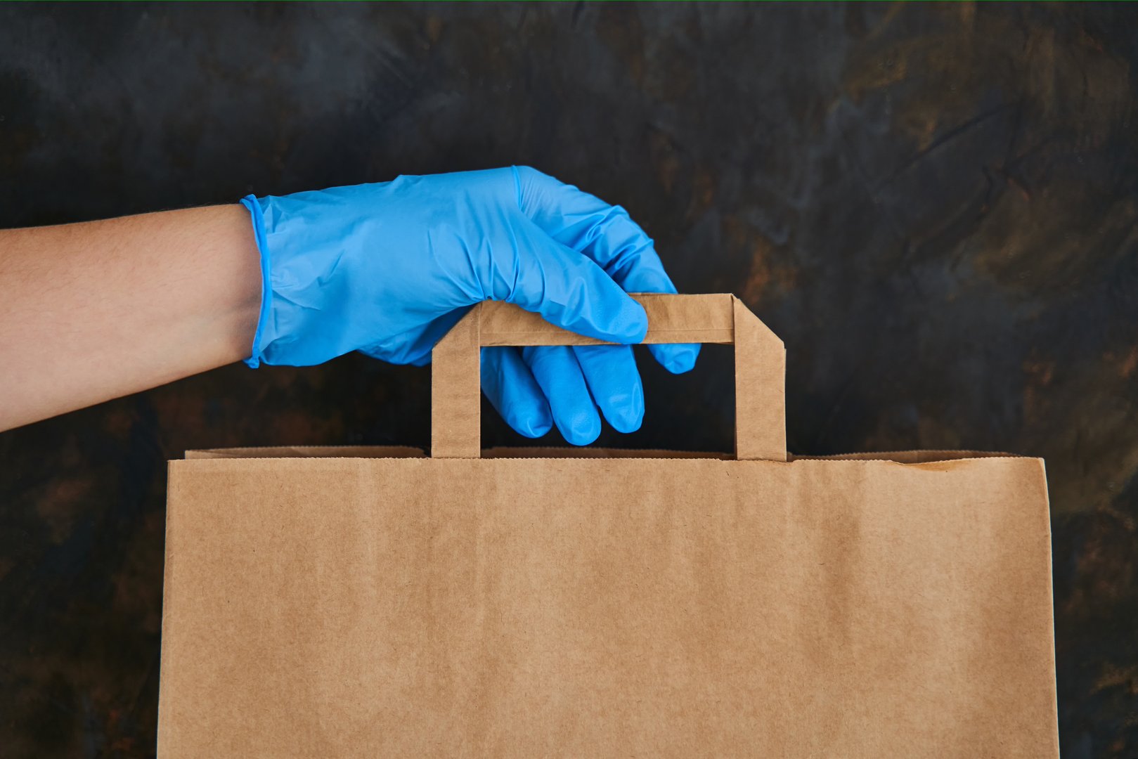 Food donation box. Woman delivering food in paper bag during Covid 19 outbreak. Girl holds a paper bag in blue gloves. Coronavirus Prevention.
