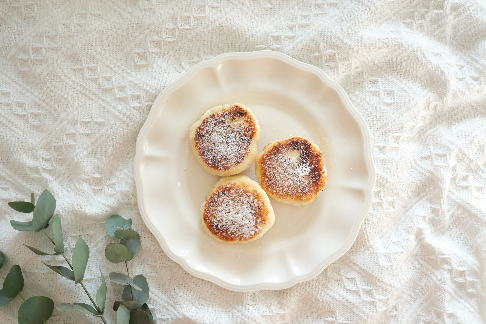 On an elegant and beautiful plate, there are three baked cheesecake that are generously topped with coconut on white fabric.