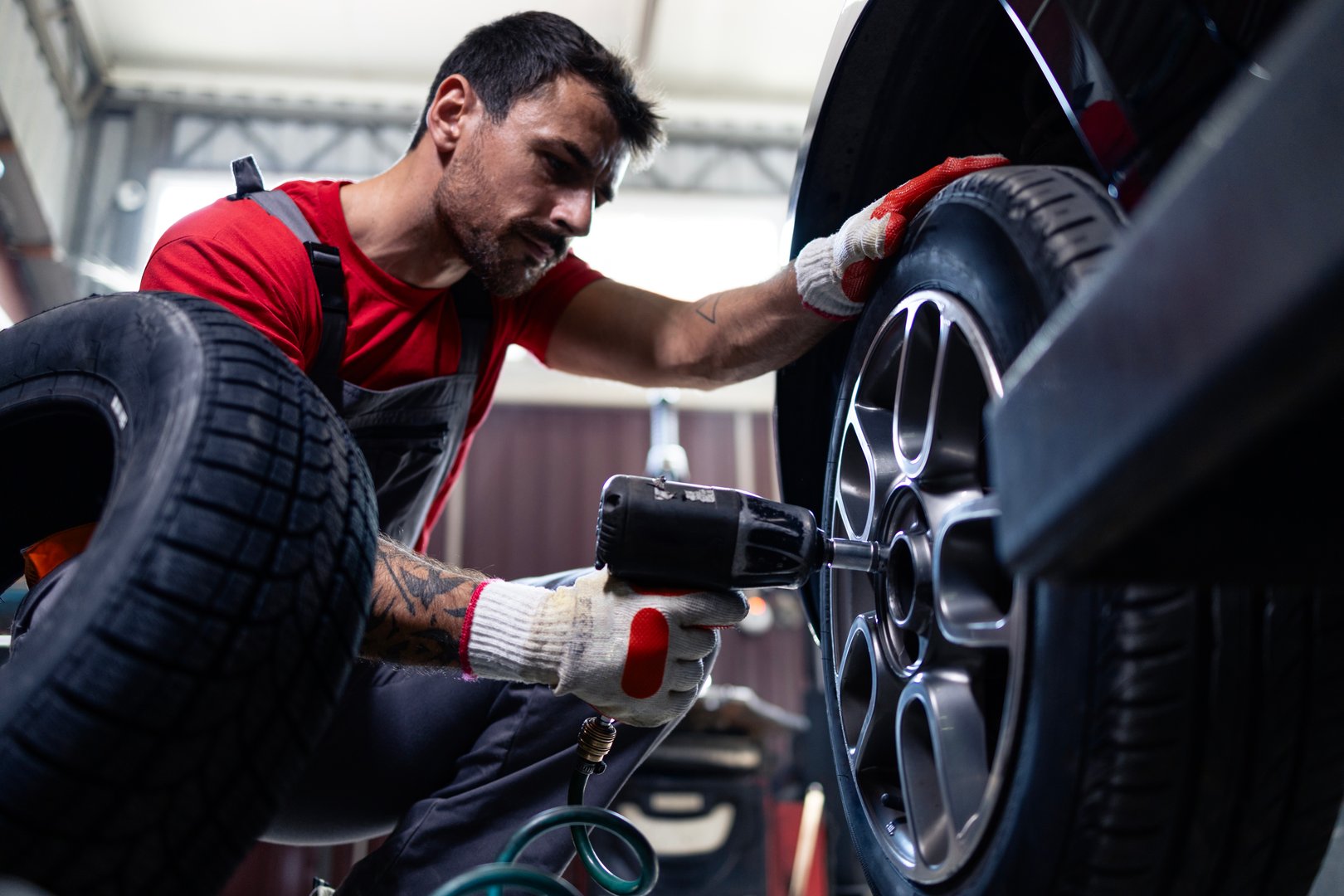 Mechanic removing wheels from vehicle with pneumatic impact wrench tool inside workshop.