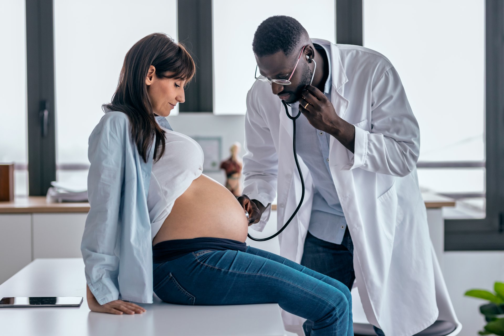 Shot of smart male obstetrician doctor with stethoscope listening to beautiful pregnant woman baby heartbeat.