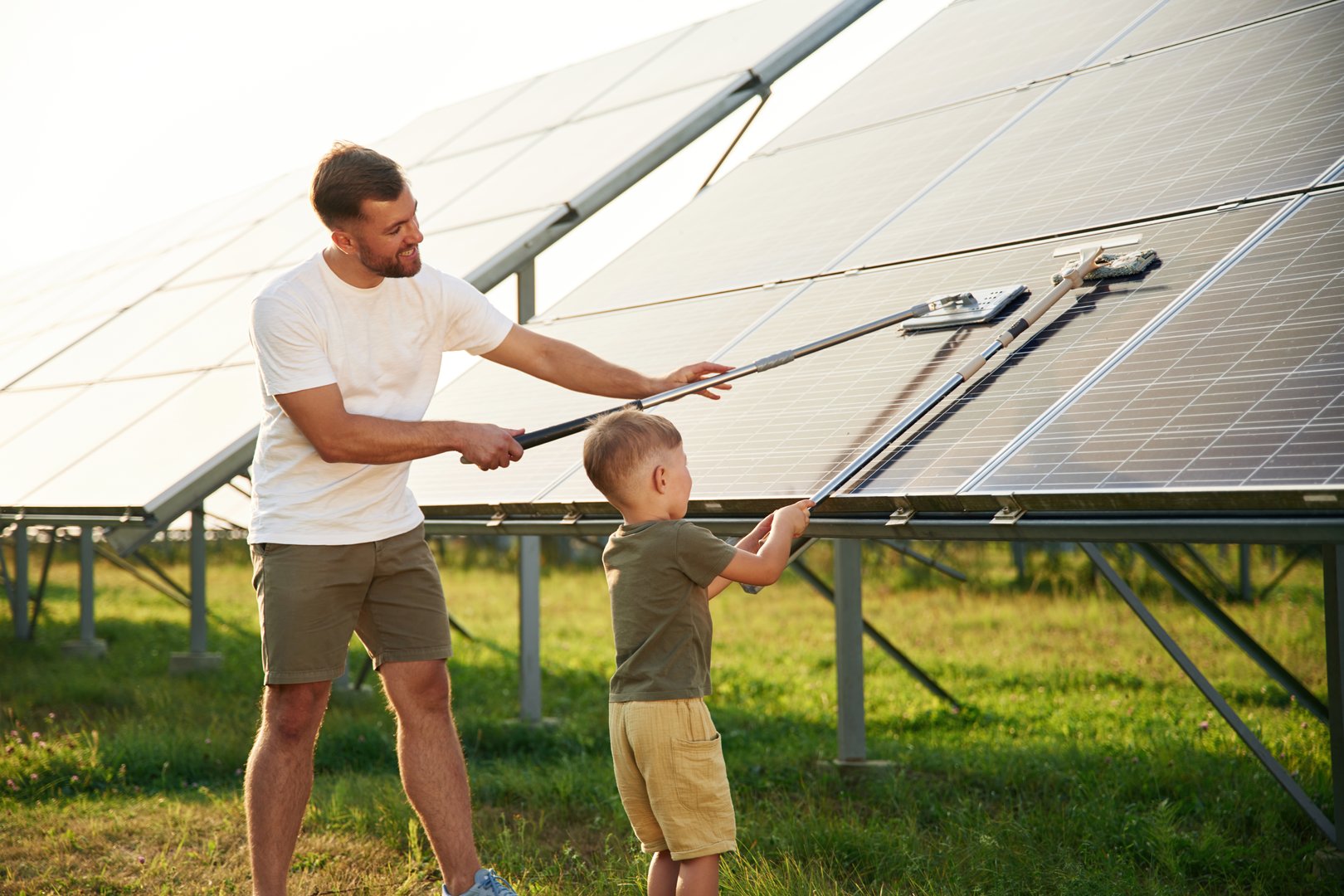 Cleaning the surface. Father with his little son are together near the solar panels.