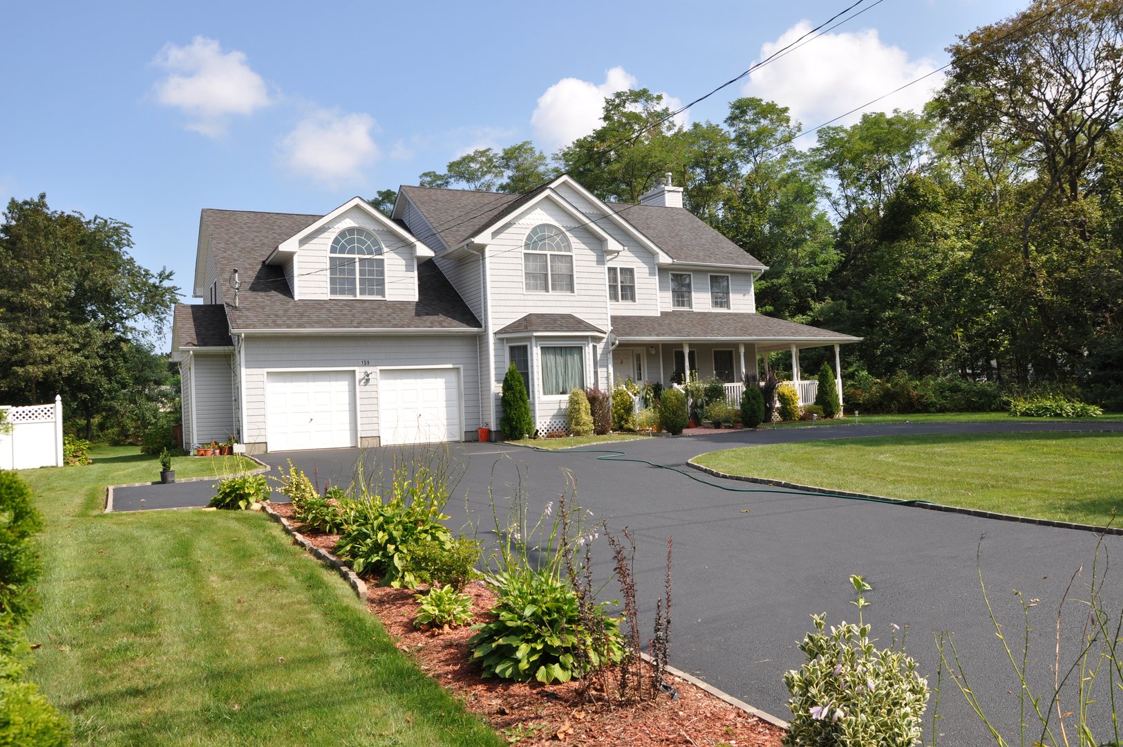 Suburban home with long blacktop driveway flower bed two car garage on sunny blue cloud sky day in residential neighborhood