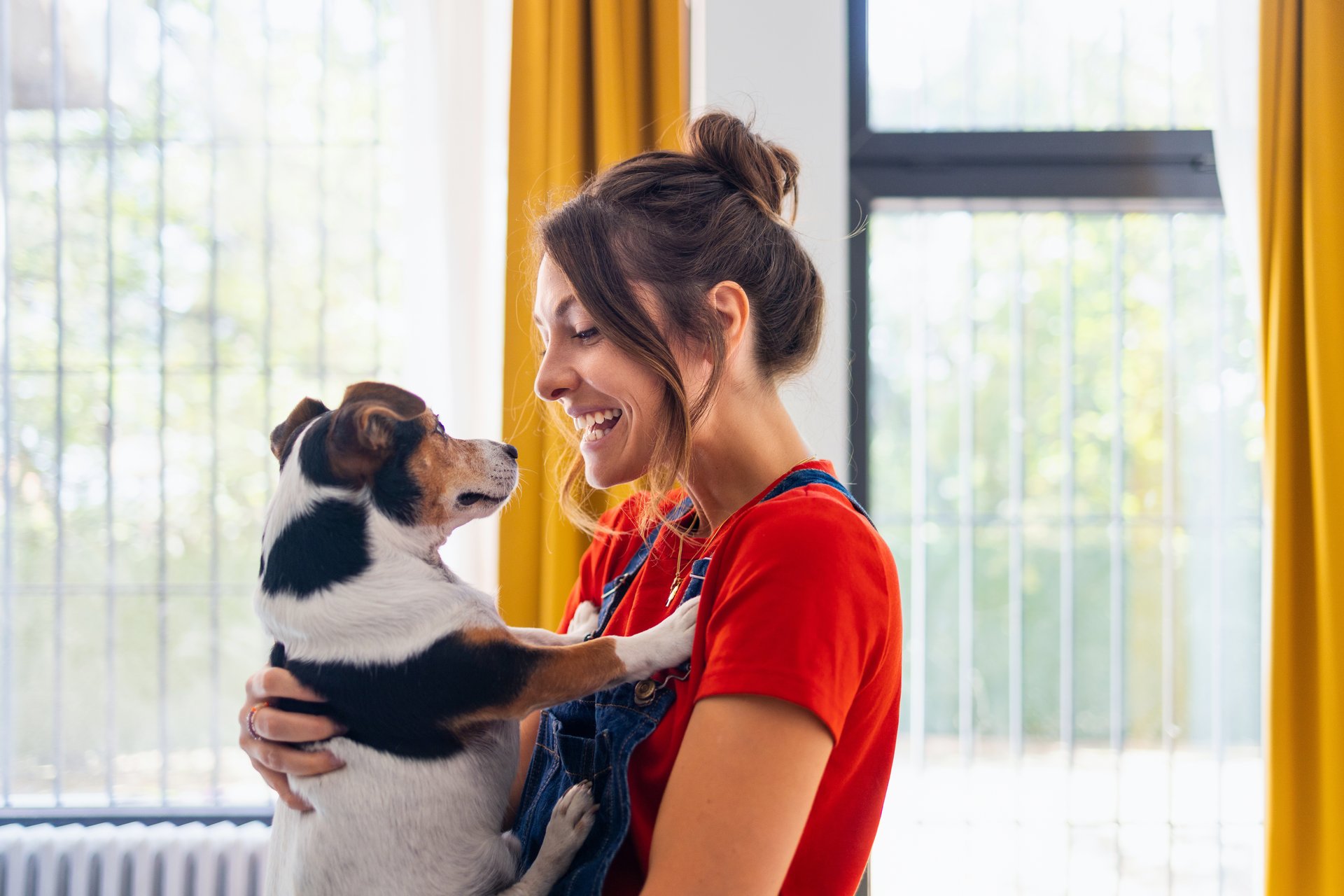 A joyful woman interacts with her dog indoors. The bright setting indicates a cheerful, positive environment. The moment captures affection, happiness, and companionship between the person and the animal.