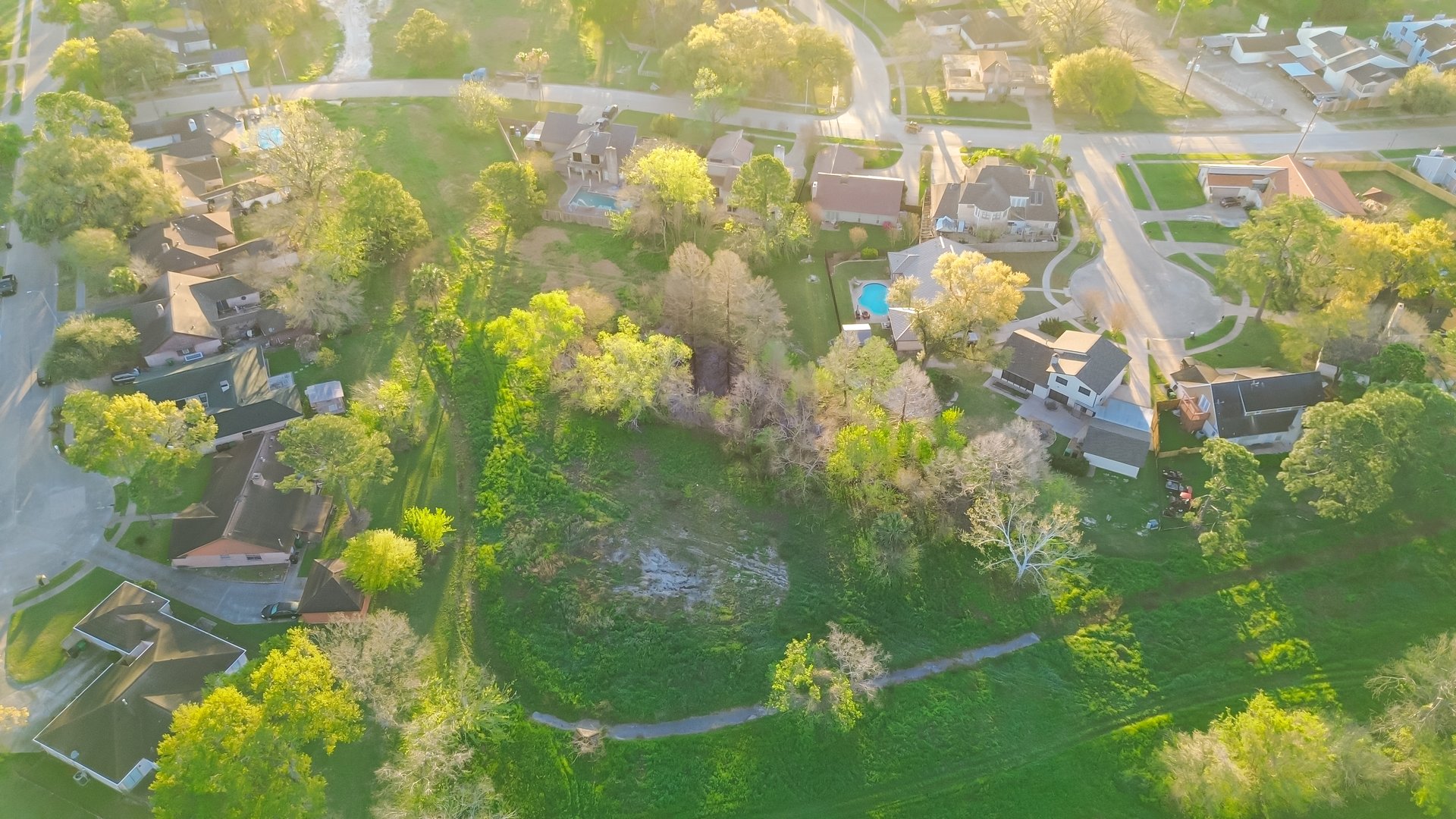Park side residential neighborhood with cul-de-sac dead-end street, lush green trees and grass lined drainage channel