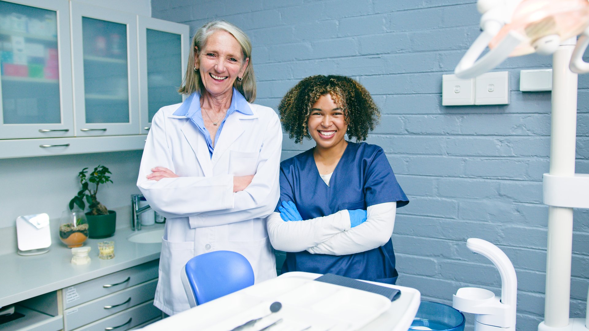 Dentists stand confidently in a well-equipped office. They wear professional uniforms and radiate a friendly attitude, representing teamwork, healthcare, and exceptional dental services amid a clean, modern clinic setting.